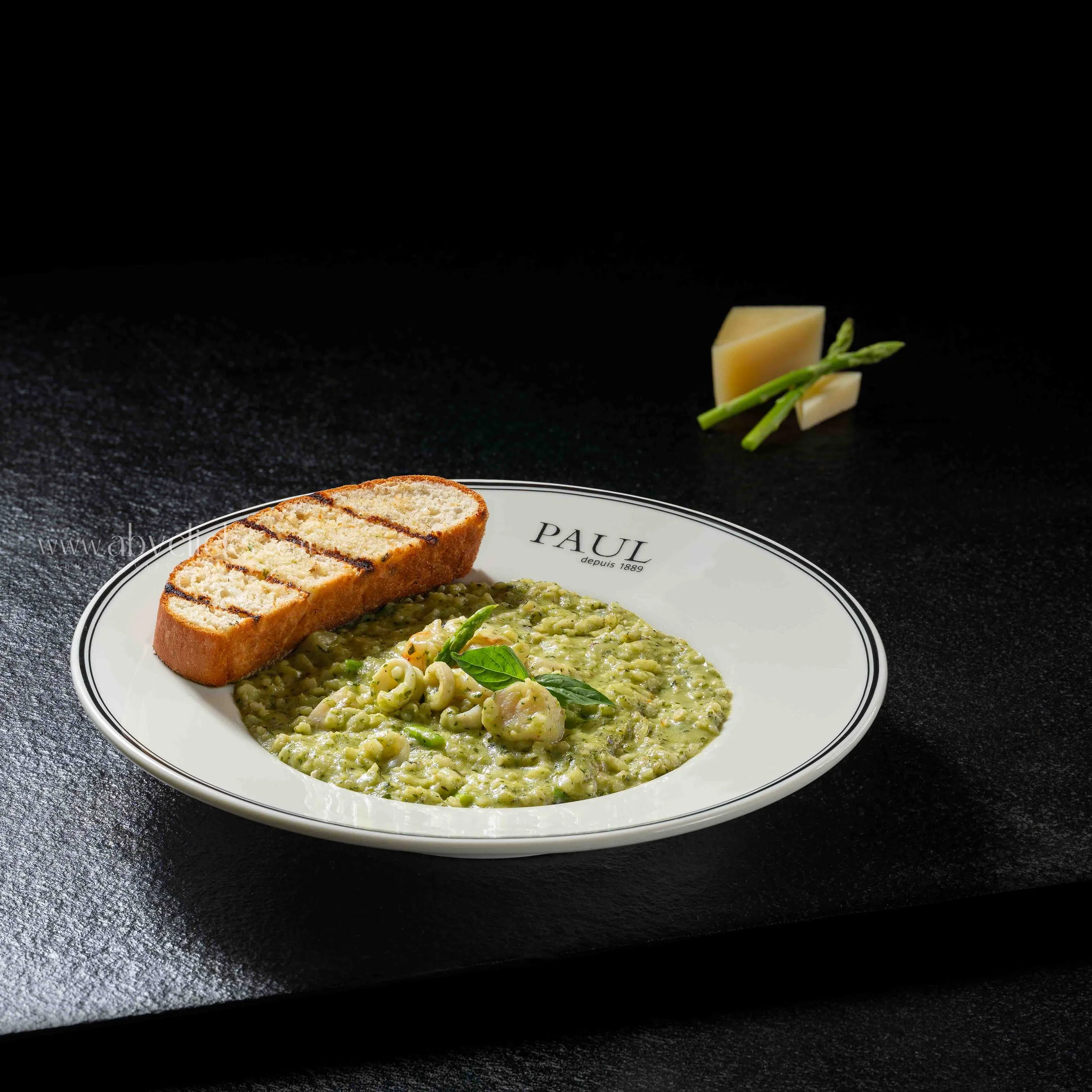 A plate of food with grilled bread, green salad, and a creamy pasta dish with green herbs, on a black surface.