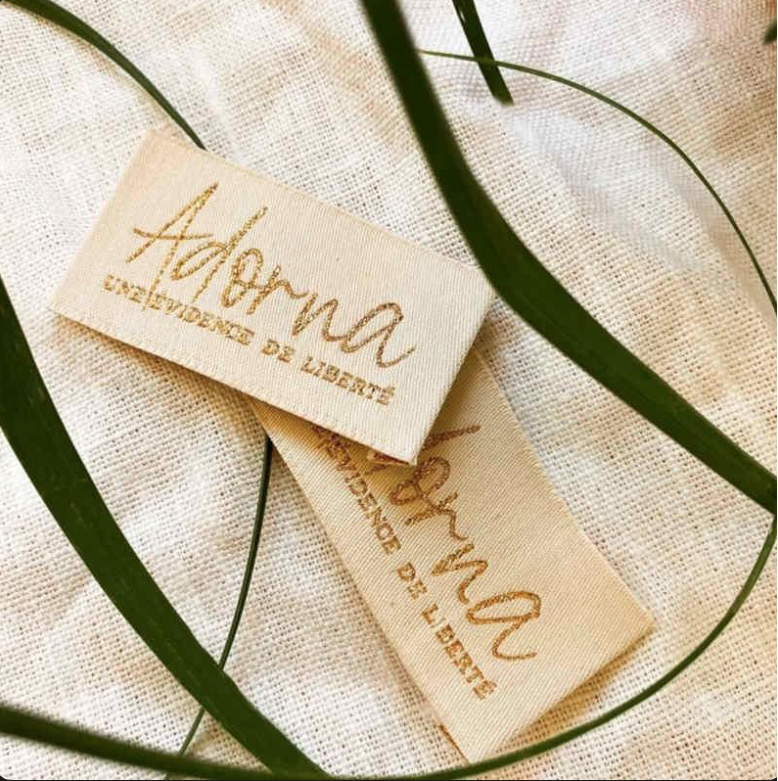 Two beige fabric tags with gold lettering that says "Abyss" and "Aloe Vera" are placed on a light woven fabric. Green plant leaves frame the tags.