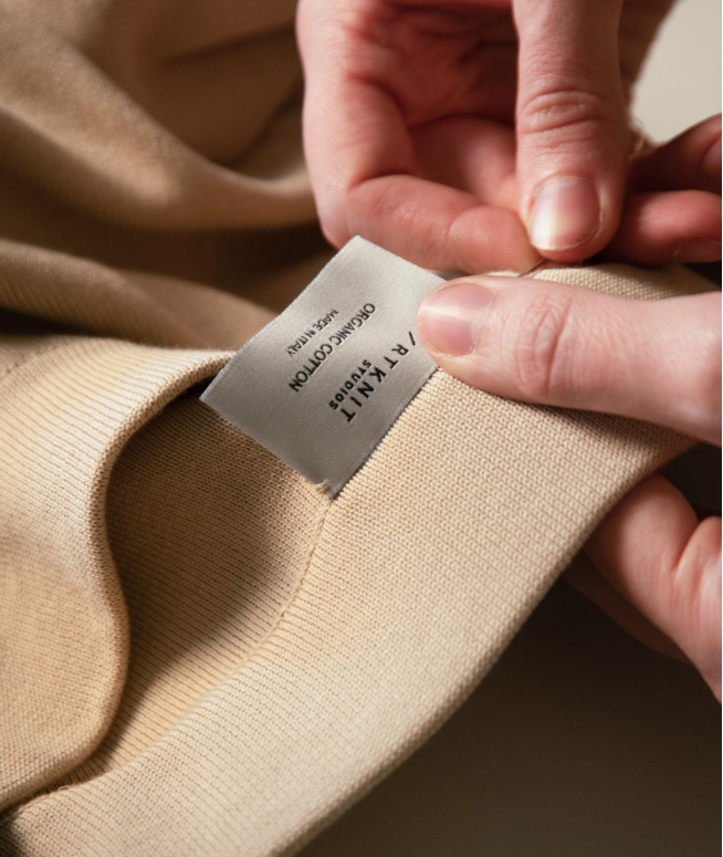 Close-up of a person's hands holding a beige fabric clothing label that reads 'TEXLI FIT & SEW ORIGINAL COTTON MADE IN VIETNAM'.