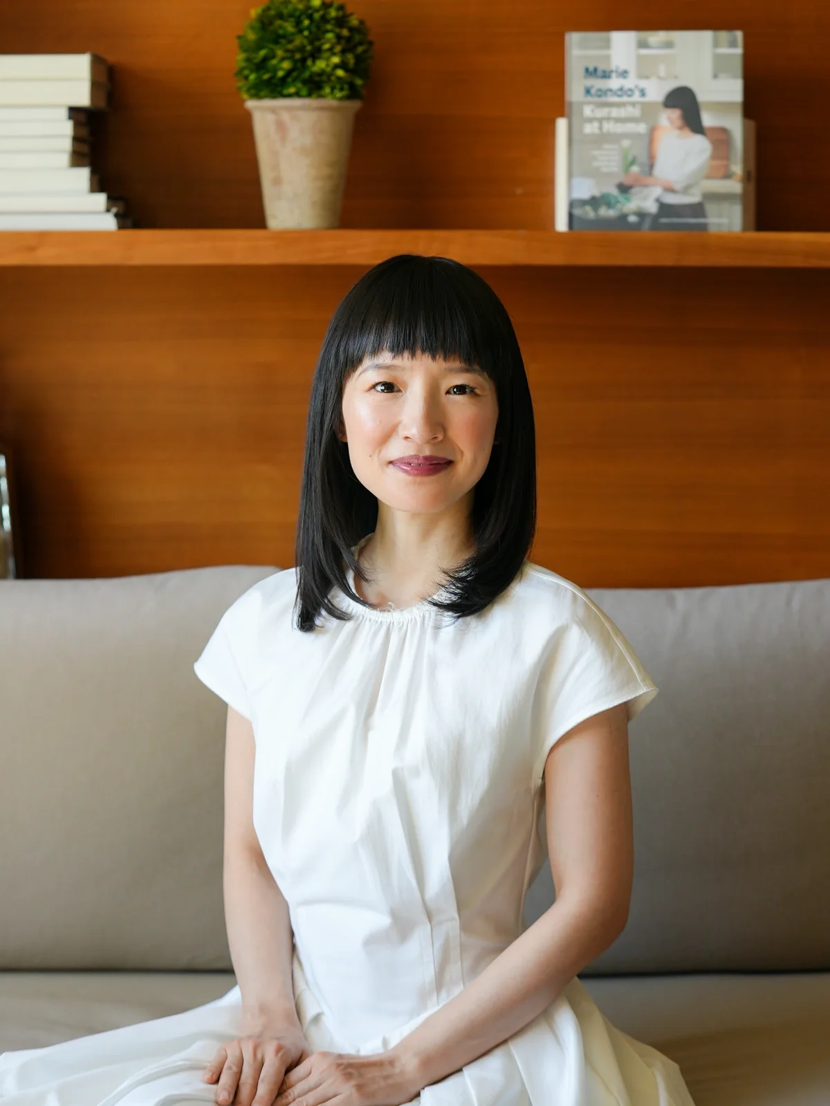 Marie Kondo seated in front of a wooden bookshelf