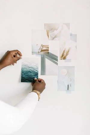 Person's hands arranging printed photographs on a white surface, with a white background.