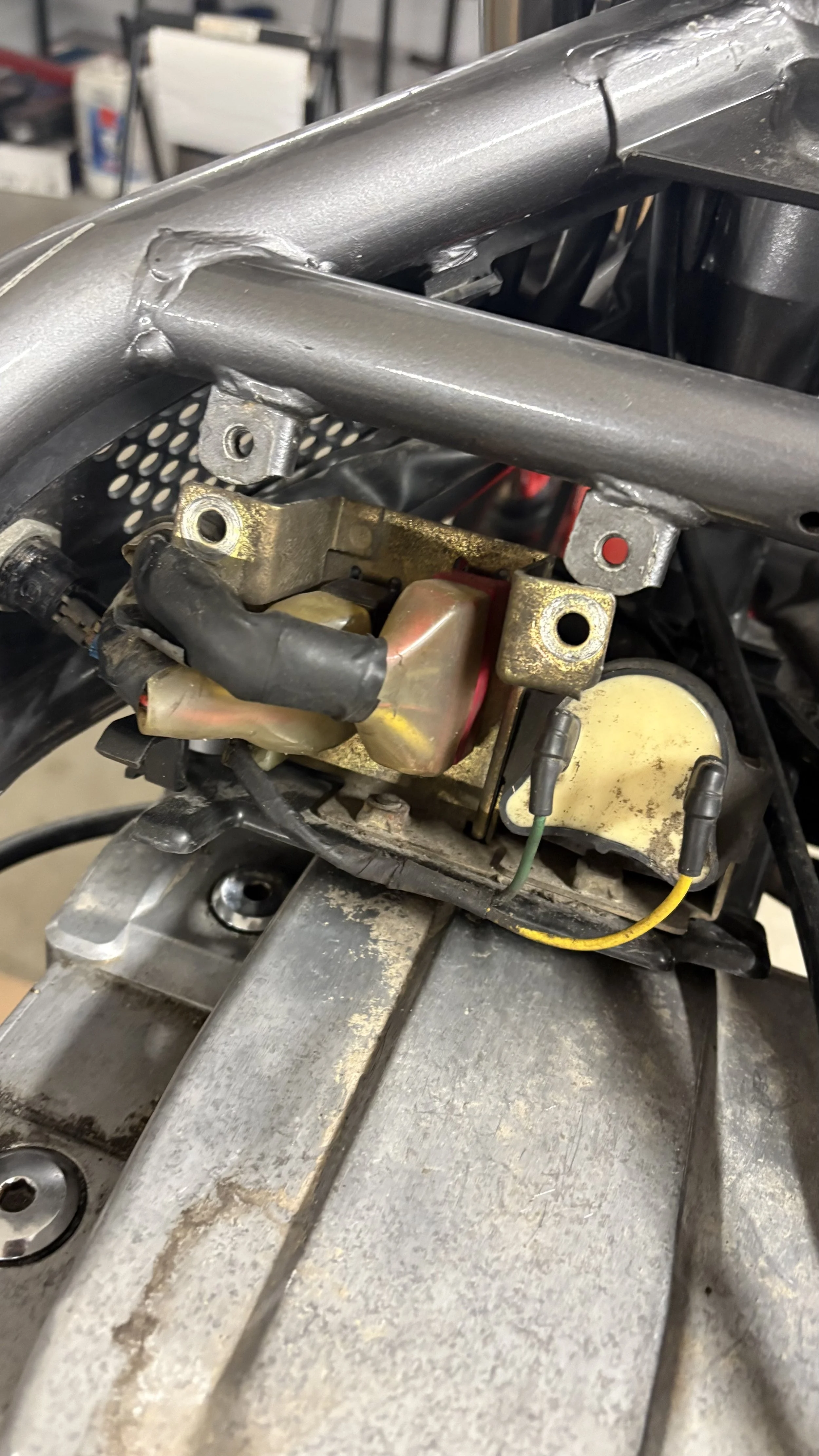 Close-up of a metallic motorcycle frame and carburetor with wires, on a workbench.