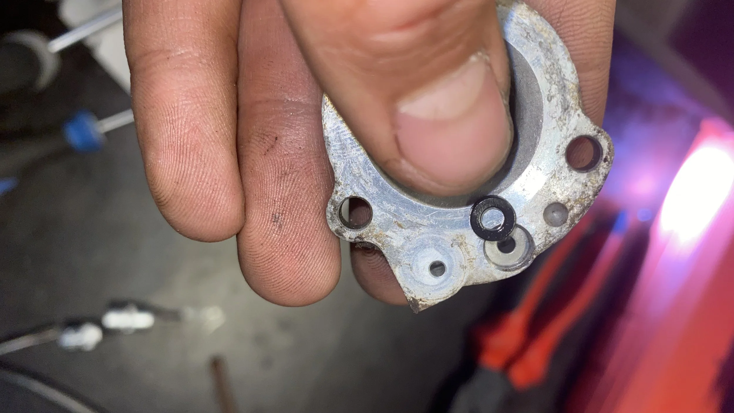 Close-up of a person's hand holding a small metal part, possibly from a motor or machine, with a background featuring a welding or cutting process with intense pink and purple light.