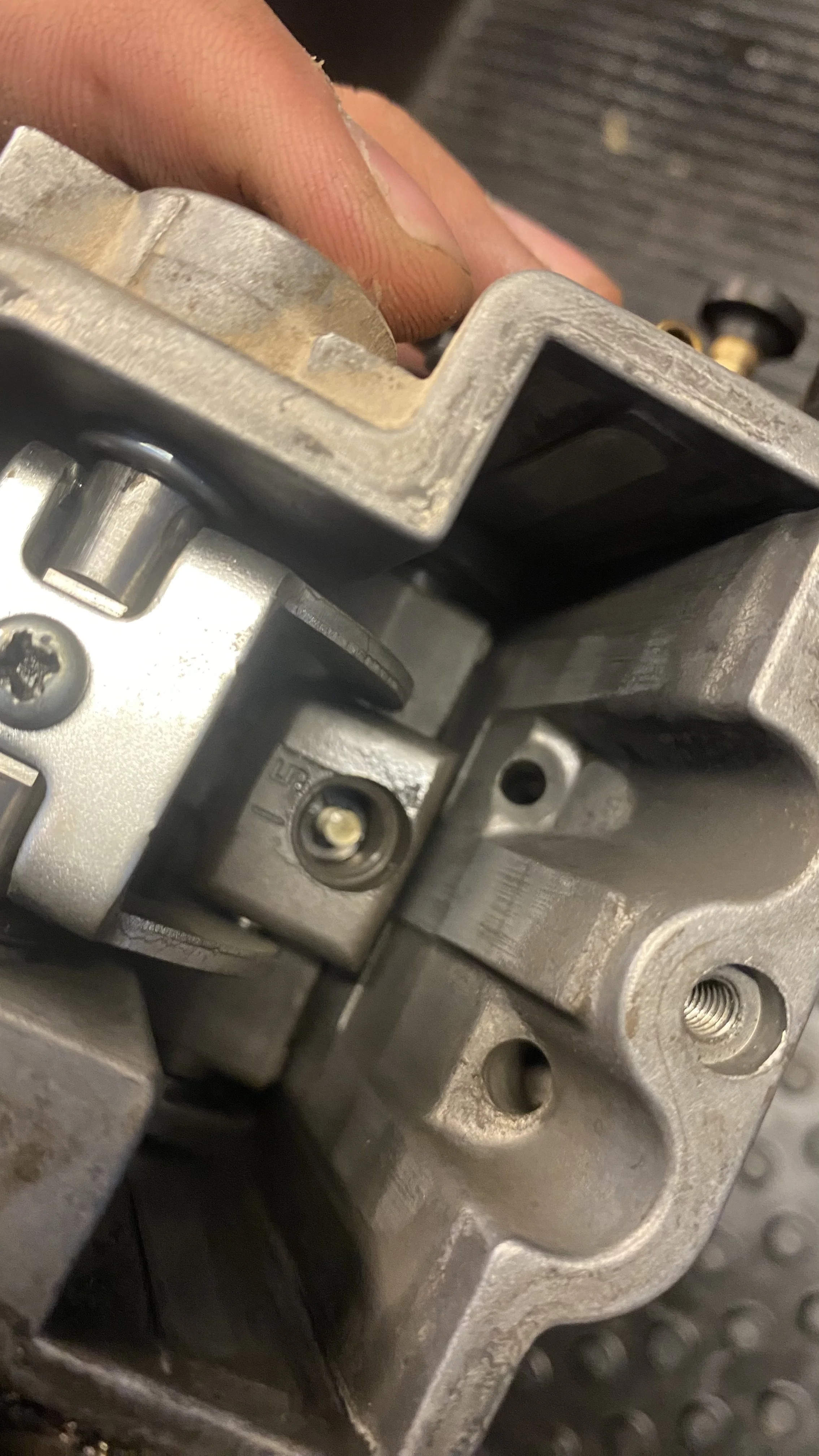 Close-up of a metallic mechanical component, possibly part of an engine or machinery, with a person's fingers gently holding or working on it.