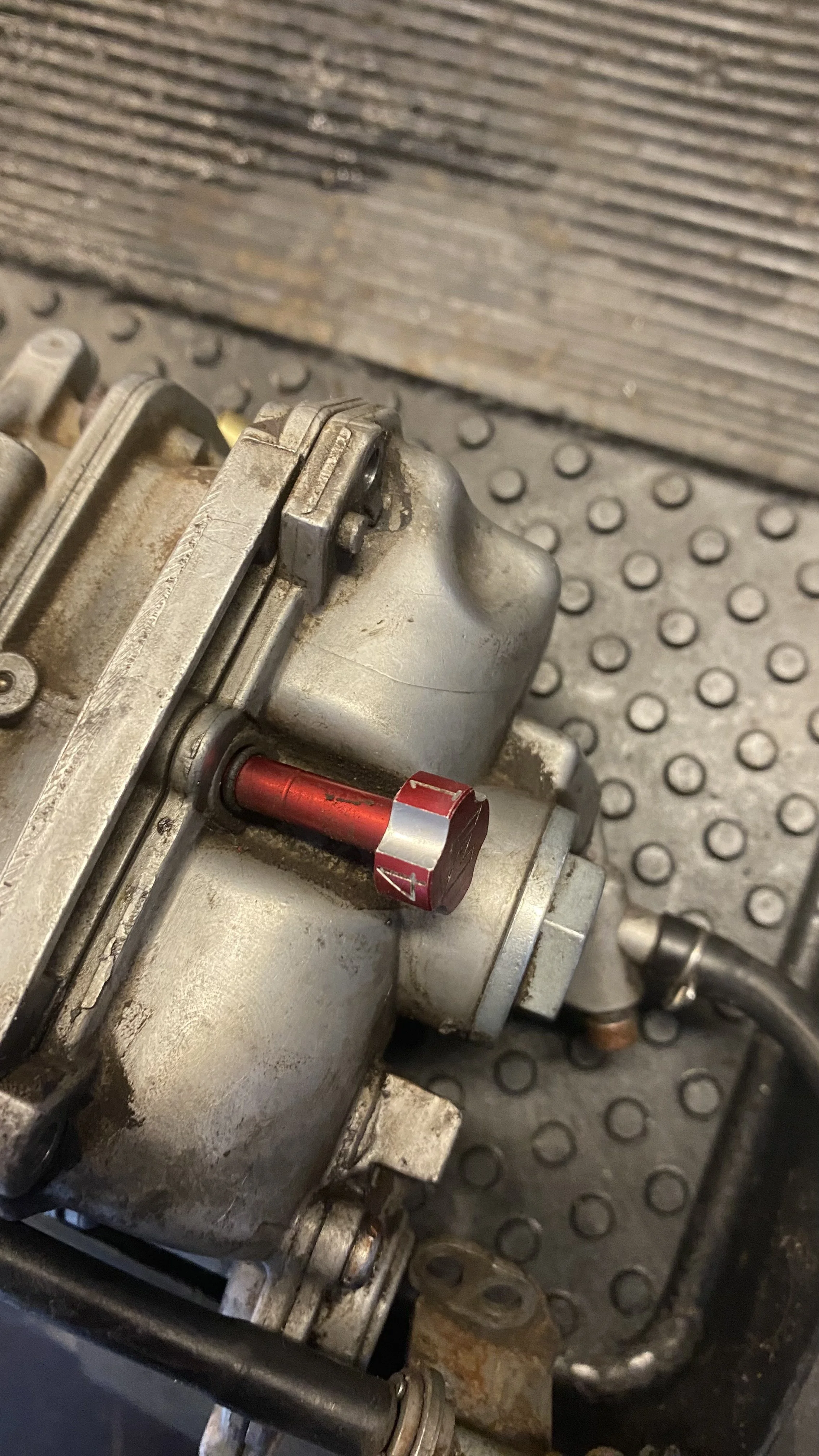 Close-up of a metallic mechanical component with a red screw, mounted on a textured black surface.