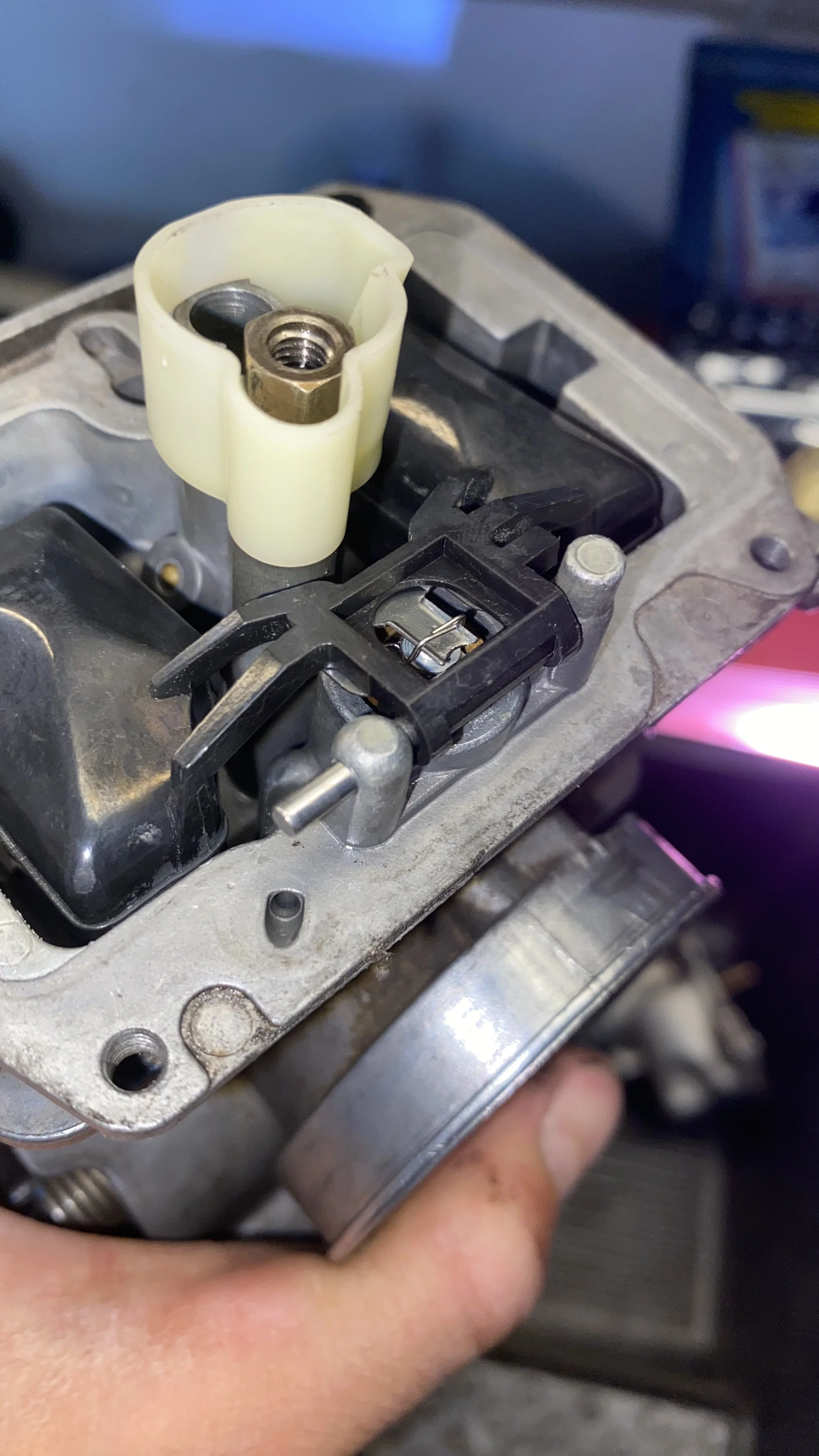Close-up of a mechanical component in a small engine, with a black plastic part and an off-white plastic piece with a threaded metal insert.