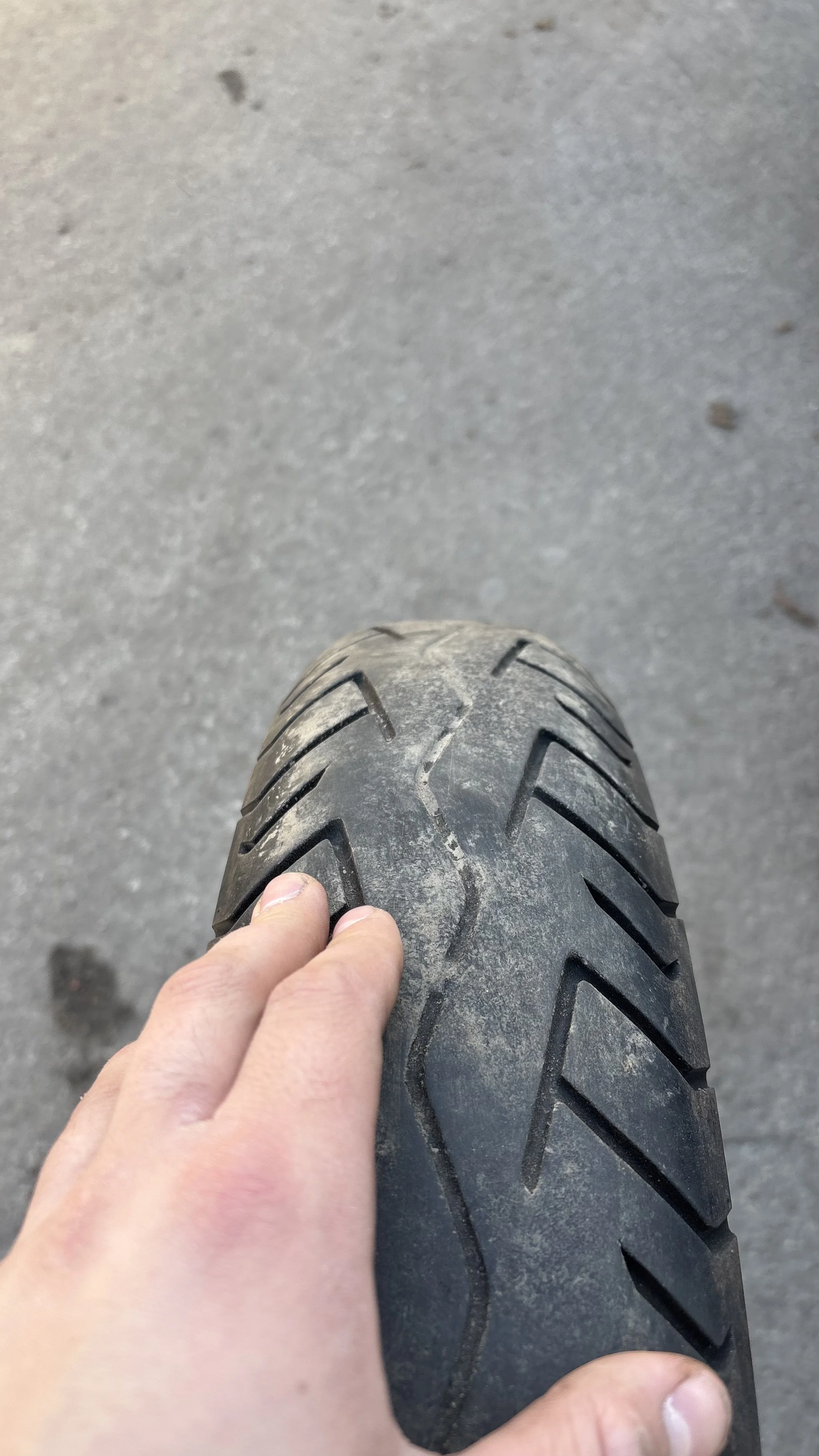 A person holding a motorcycle tire, showing the worn tread pattern.