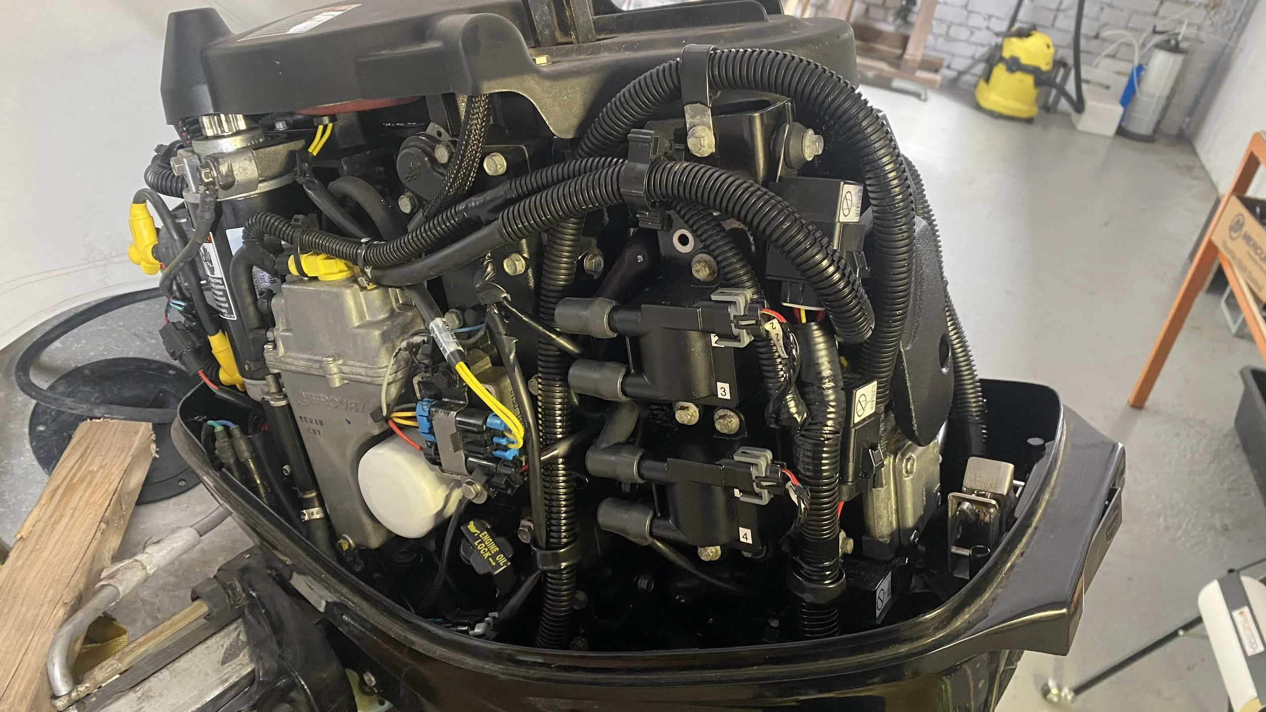 A close-up view of a boat motor engine with black wiring and mechanical parts, set on a workbench in a garage.