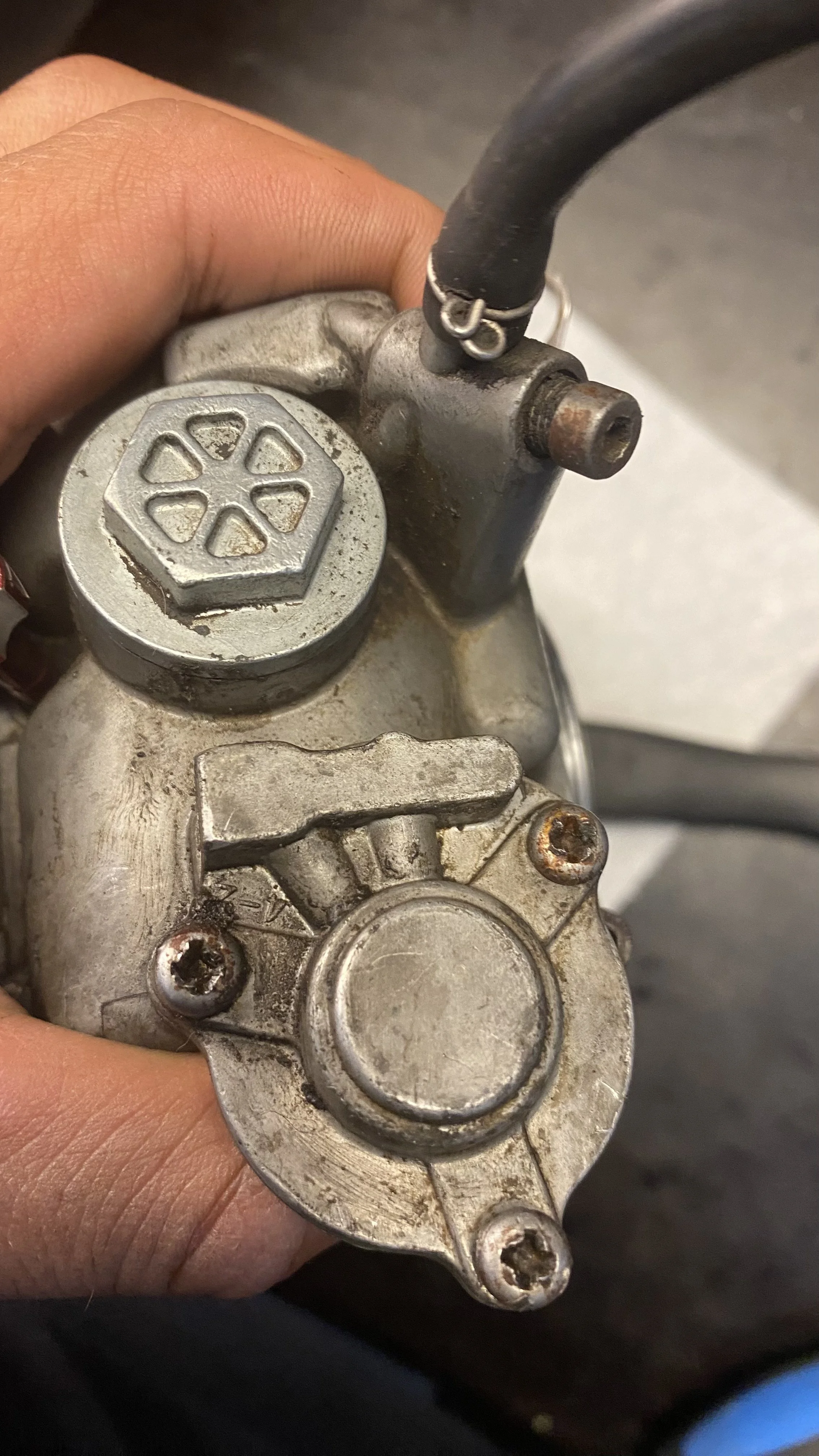 Close-up of a person's hand holding a motorcycle carburetor.