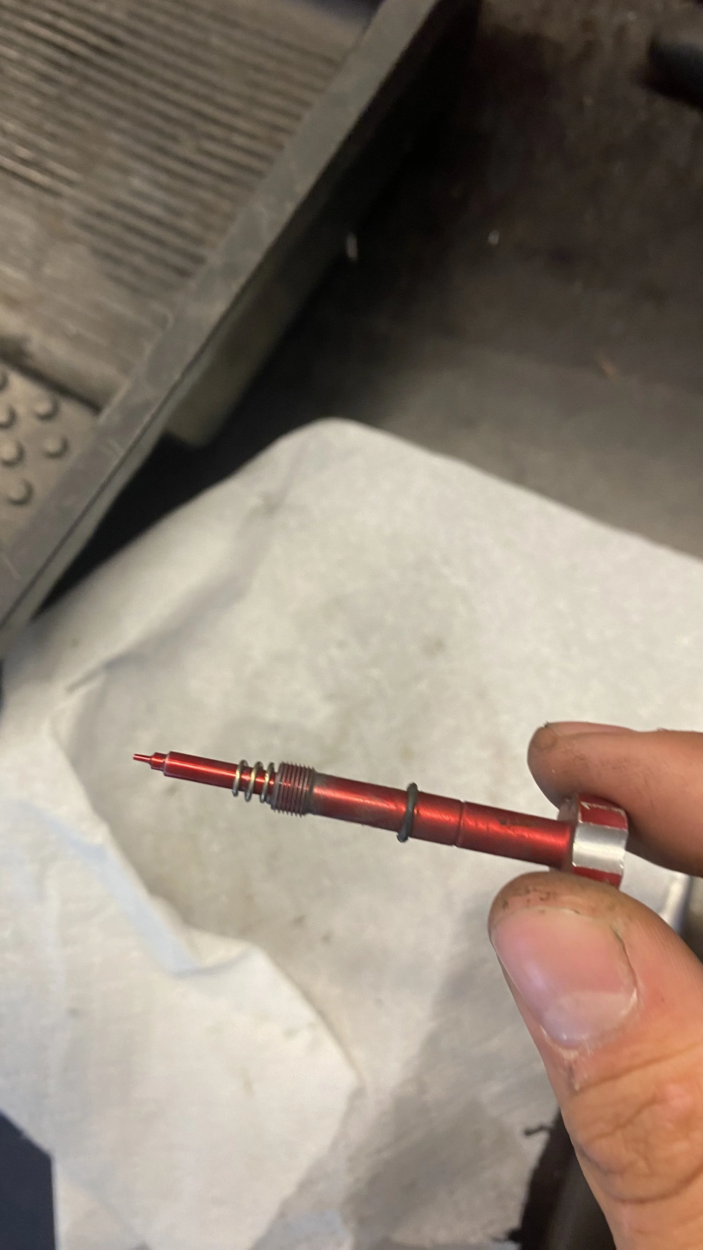 Close-up of a person's hand holding a red and silver tool with a pointed tip, near a piece of machinery or equipment.