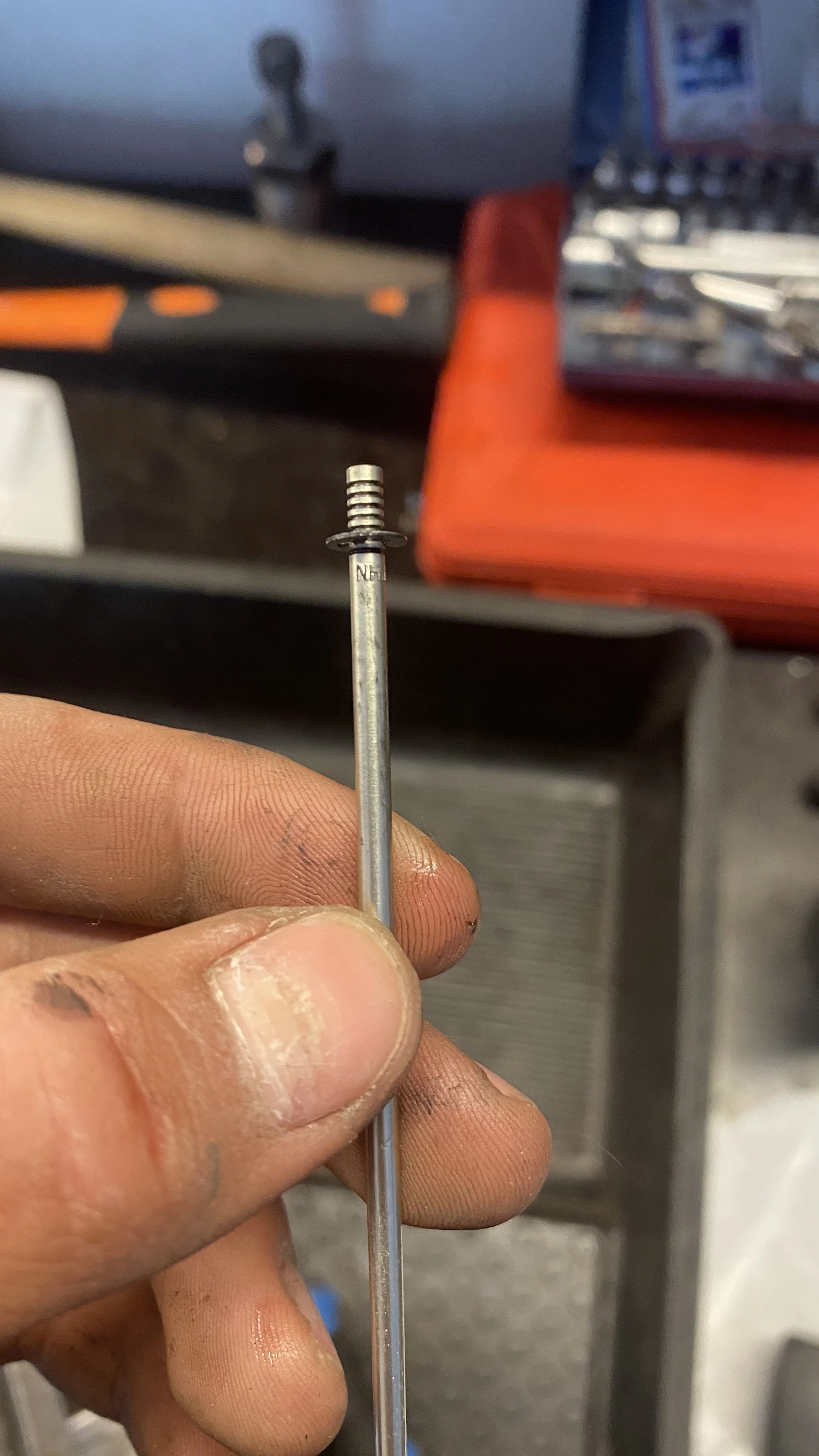 A person's hand holding a small metal rod with a small spring on top, in a workshop setting.