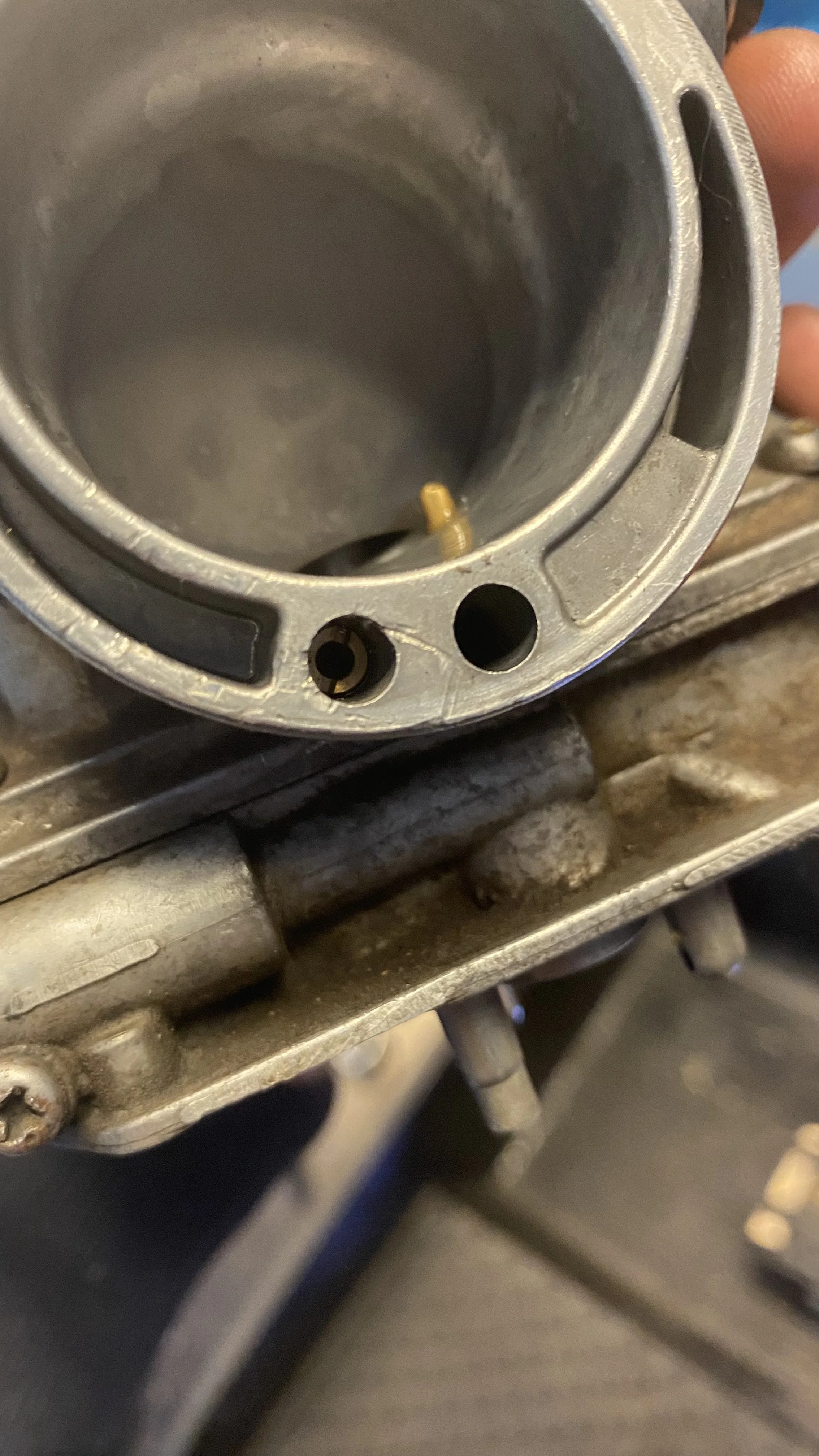 Close-up of a metallic engine part with small holes and a yellow screw.