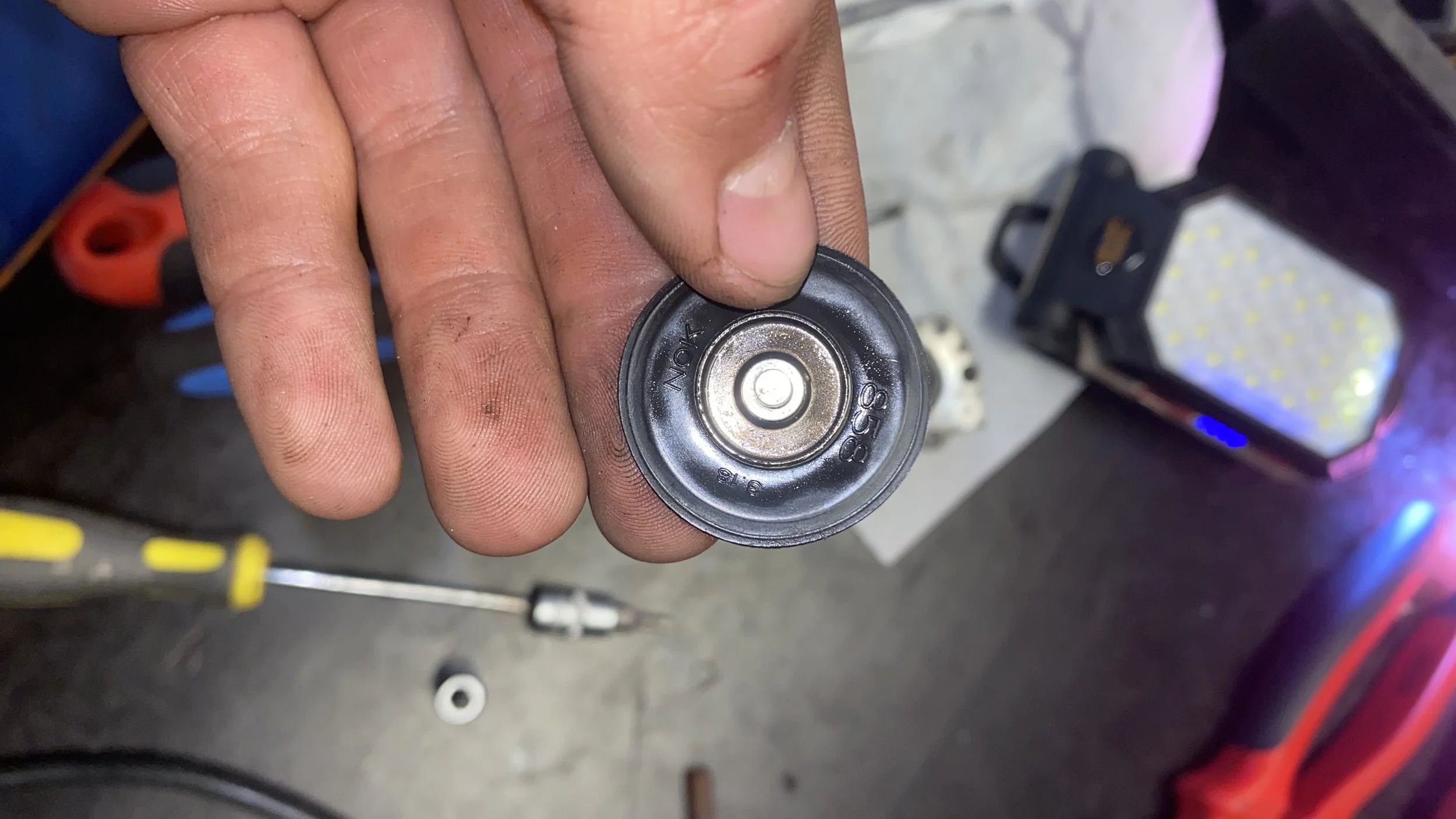 Close-up of a person's hand holding a small, round AA battery with the top side visible, showing the positive terminal and markings.