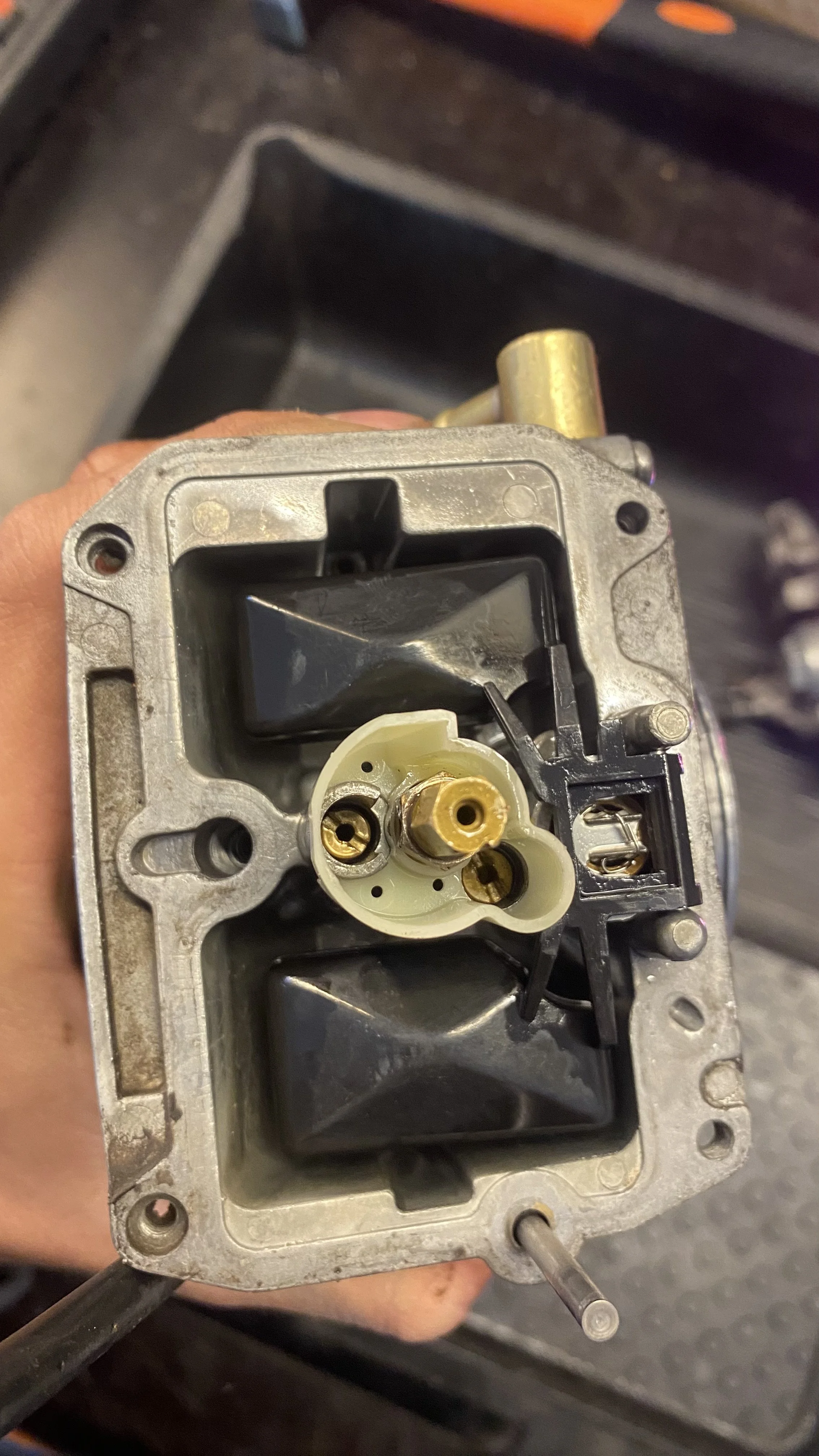 Close-up of a carburetor part with internal components visible, including brass and plastic parts.
