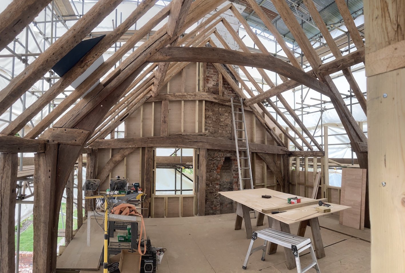 Inside of a building under construction with exposed wooden beams, a ladder, scaffolding, and construction tools.