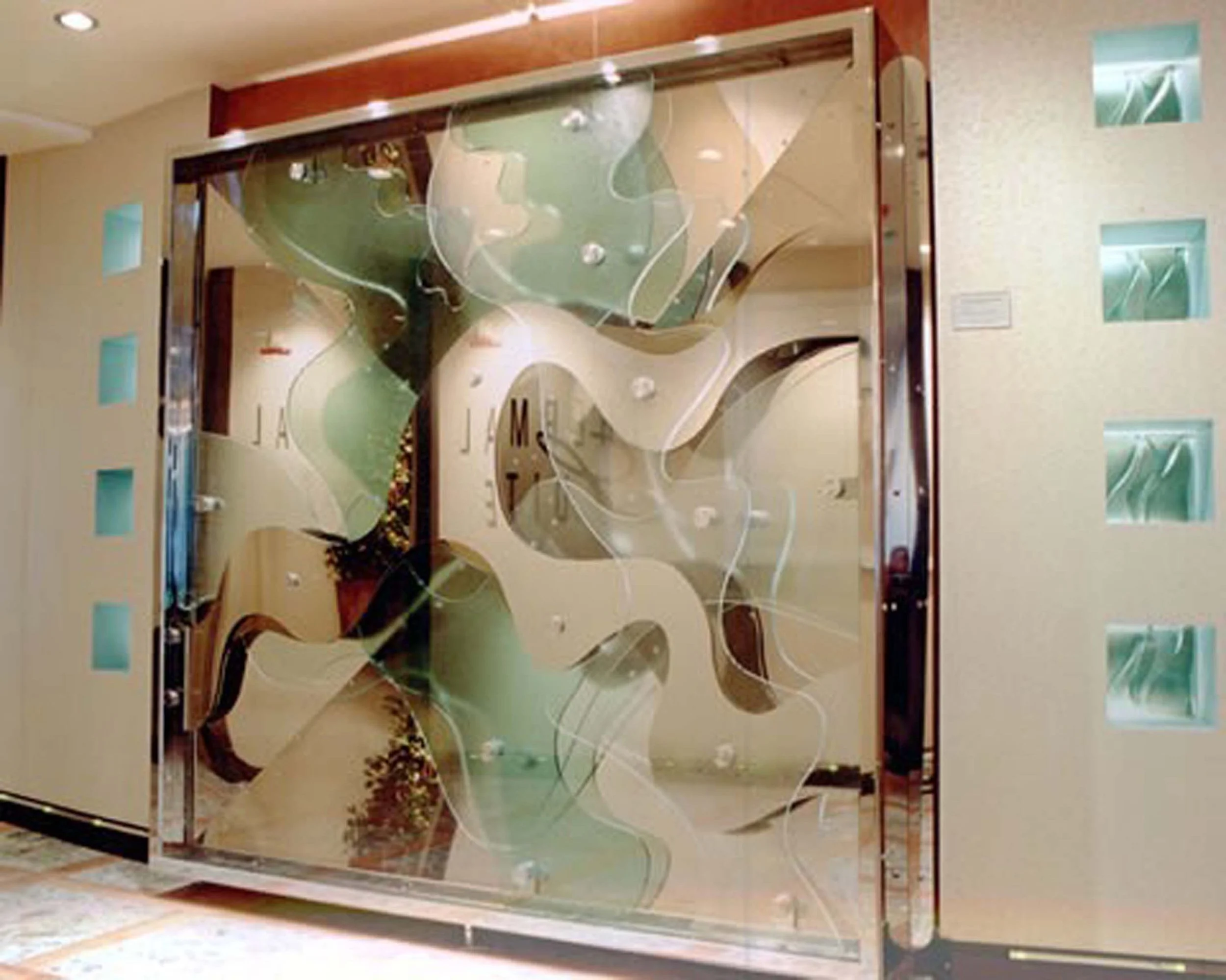 Interior view of a hotel or apartment building with beige walls, small square windows with blue glass, and a large abstract decorative glass mural featuring curved shapes and swirling lines in green, beige, and white colors.