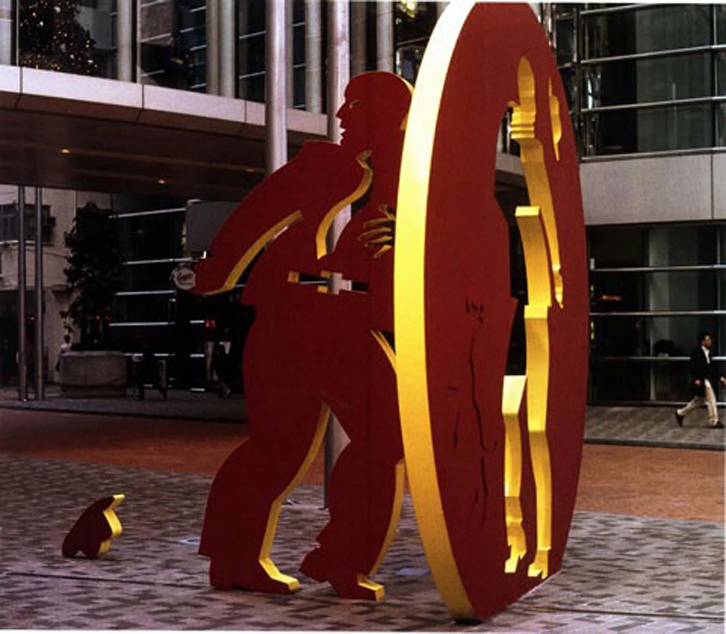 Large illuminated sculpture of a red lion with yellow accents, located outside in front of a modern building at dusk.