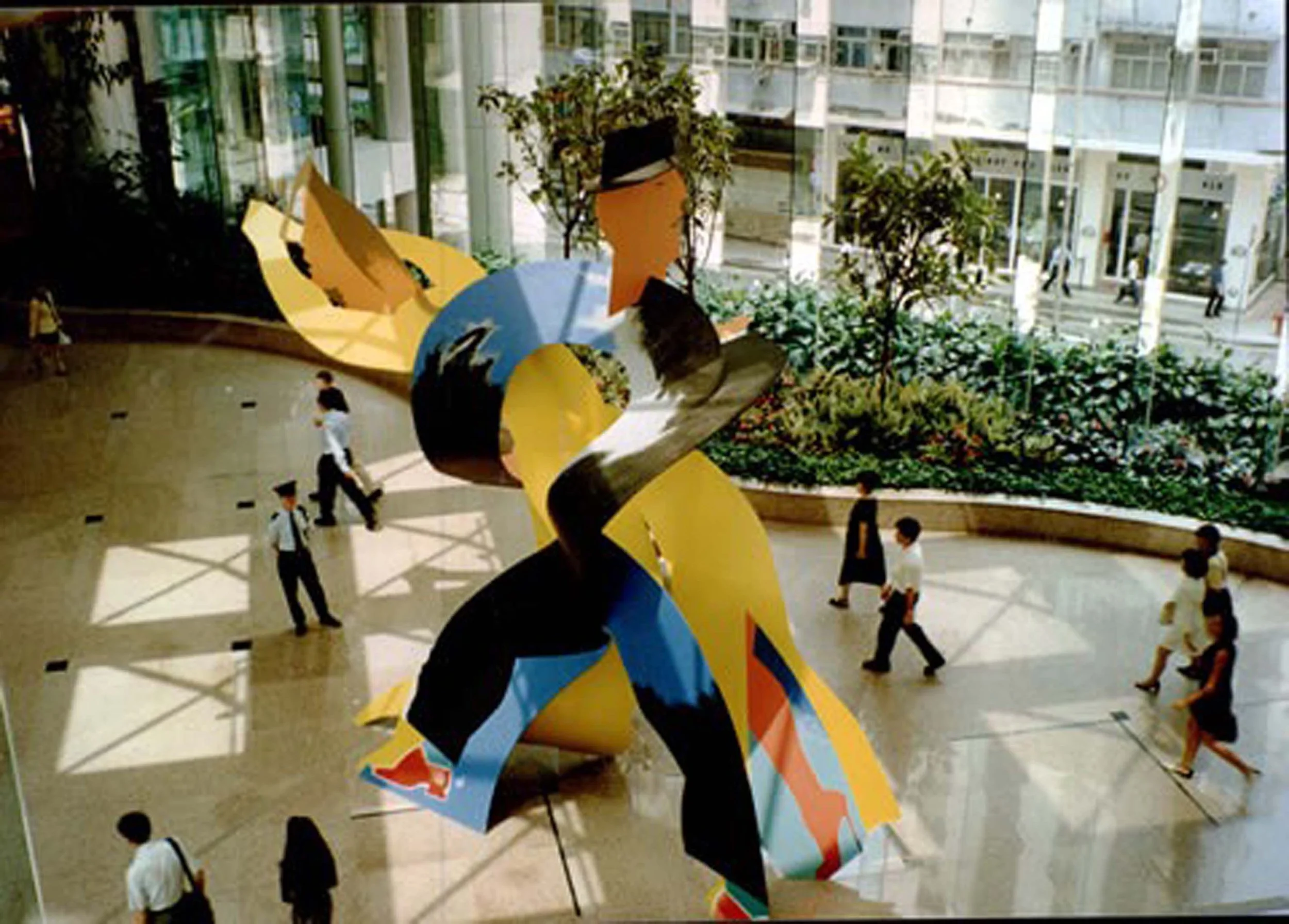 Indoor atrium with a colorful abstract sculpture, large windows, and people walking.