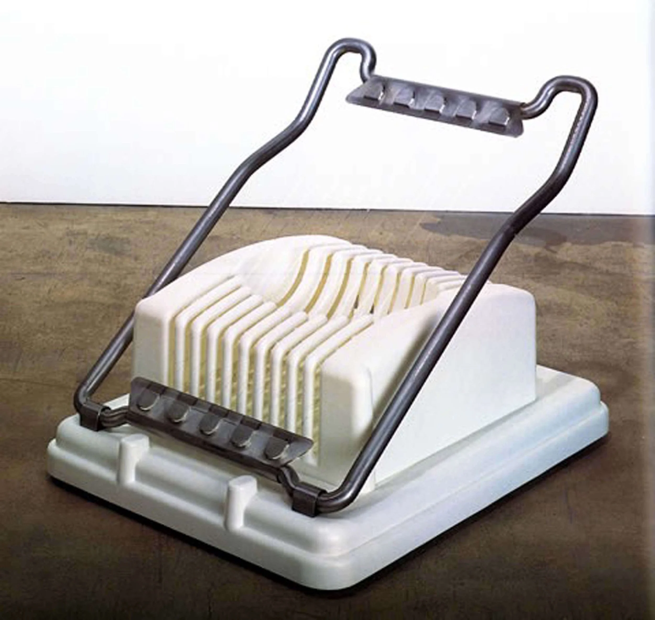 A vintage metal and white plastic clothes wringer with striped cloth between the rollers, positioned against a plain white wall.