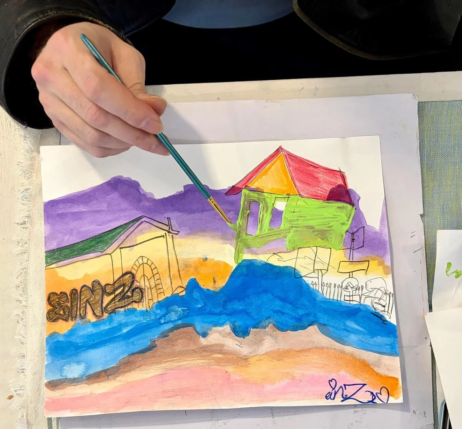A colorful watercolor painting of a coastal scene with a green house, a red and orange roof, purple mountains in the background, and blue water in the foreground. An artist's signature with hearts is visible at the bottom right.