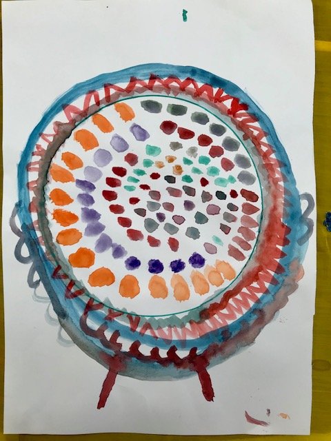 Child's colorful abstract spiral drawing with concentric circles of dots in red, orange, purple, green, and gray, on white paper with two red legs at the bottom.