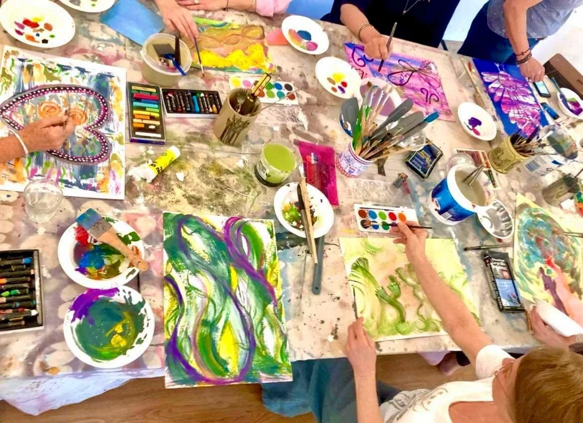 People painting colorful abstract art on paper using various paints and brushes in a group art activity.