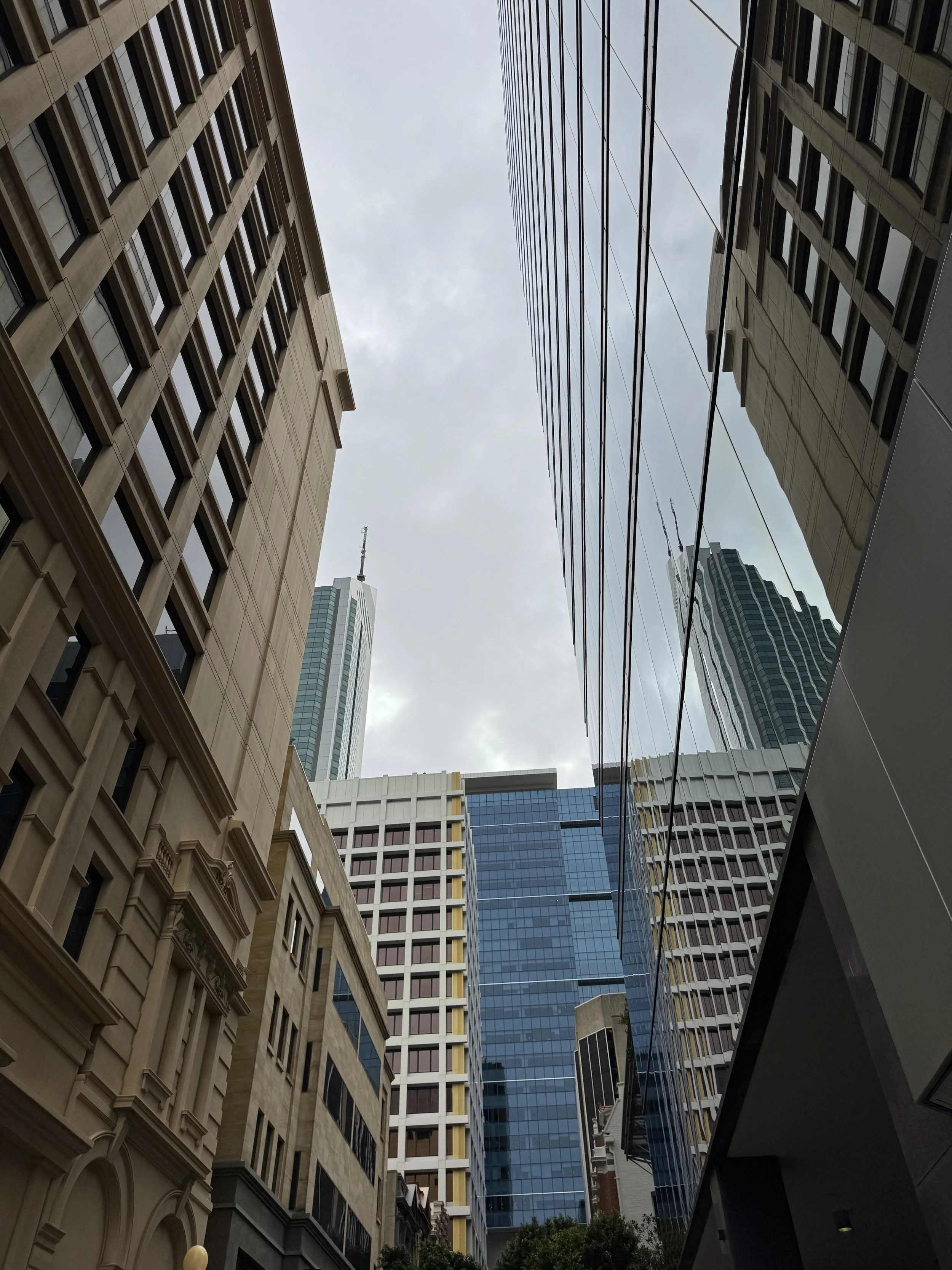 A view of tall skyscrapers and office buildings from a low angle in an urban cityscape, with overcast sky.