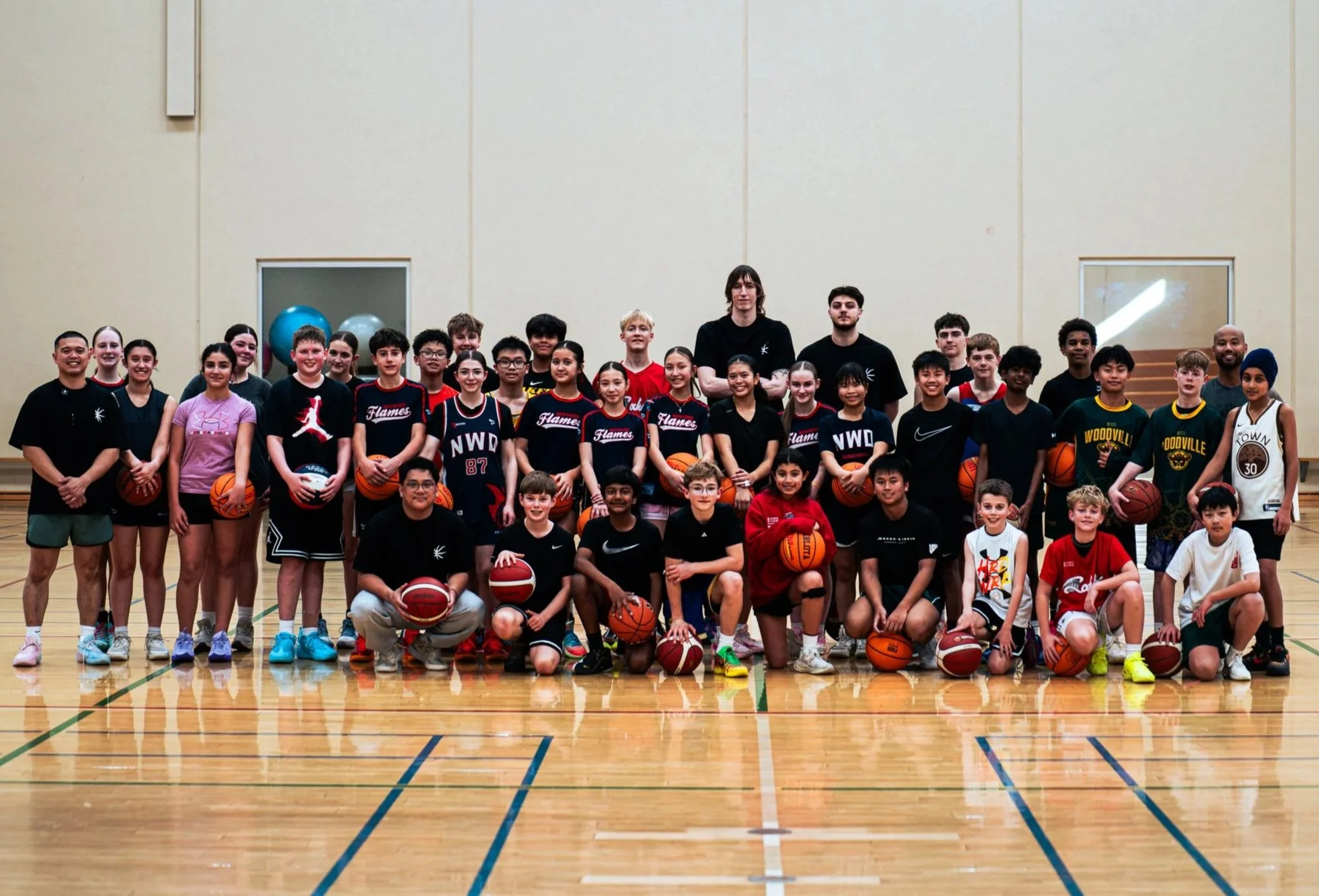 Group of young basketball players and coaches in a gymnasium, posing for a team photo with basketballs.