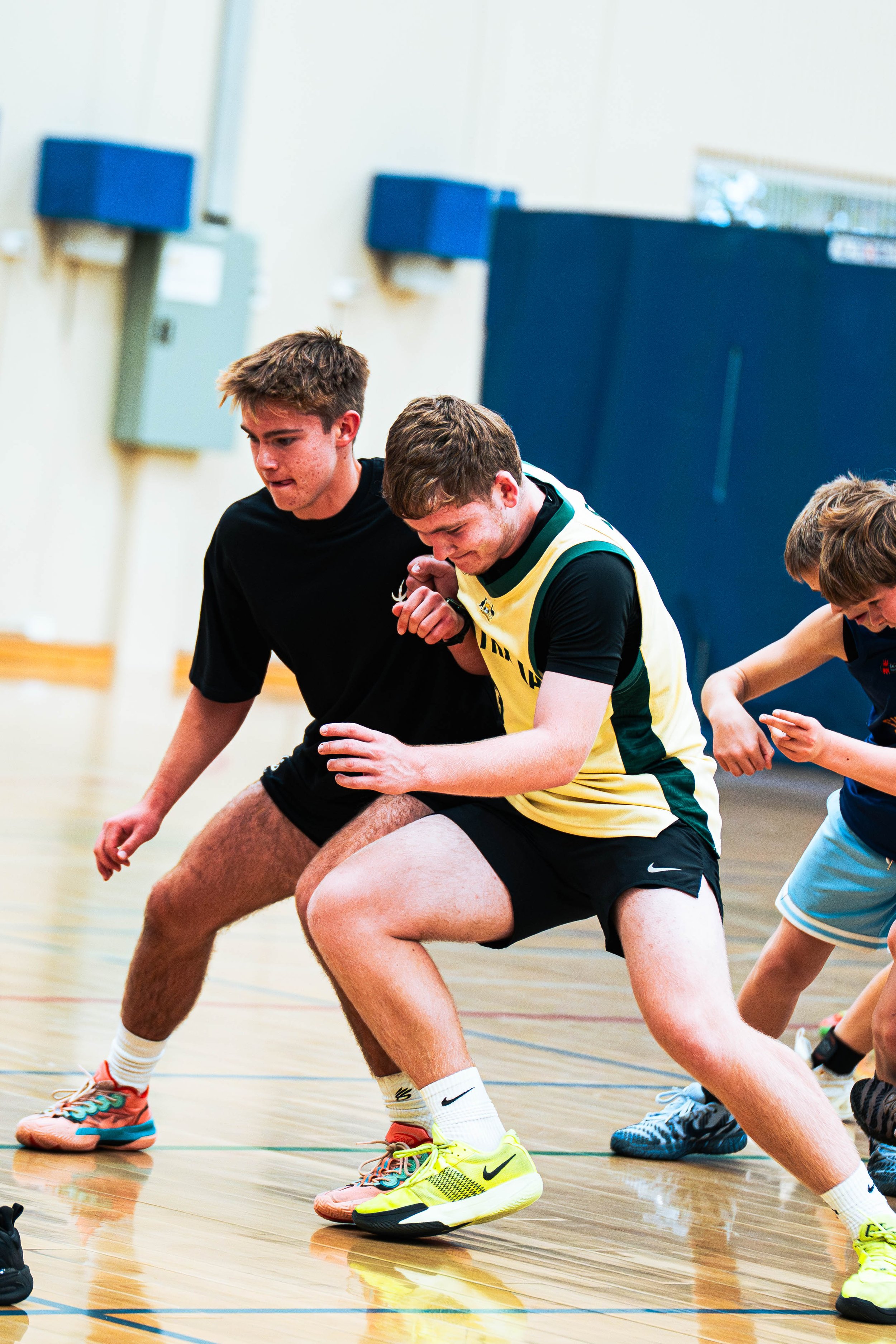 Group of teenage boys playing basketball inside a gymnasium, focusing on their legs and shoes as they crouch to defend or steal the ball.