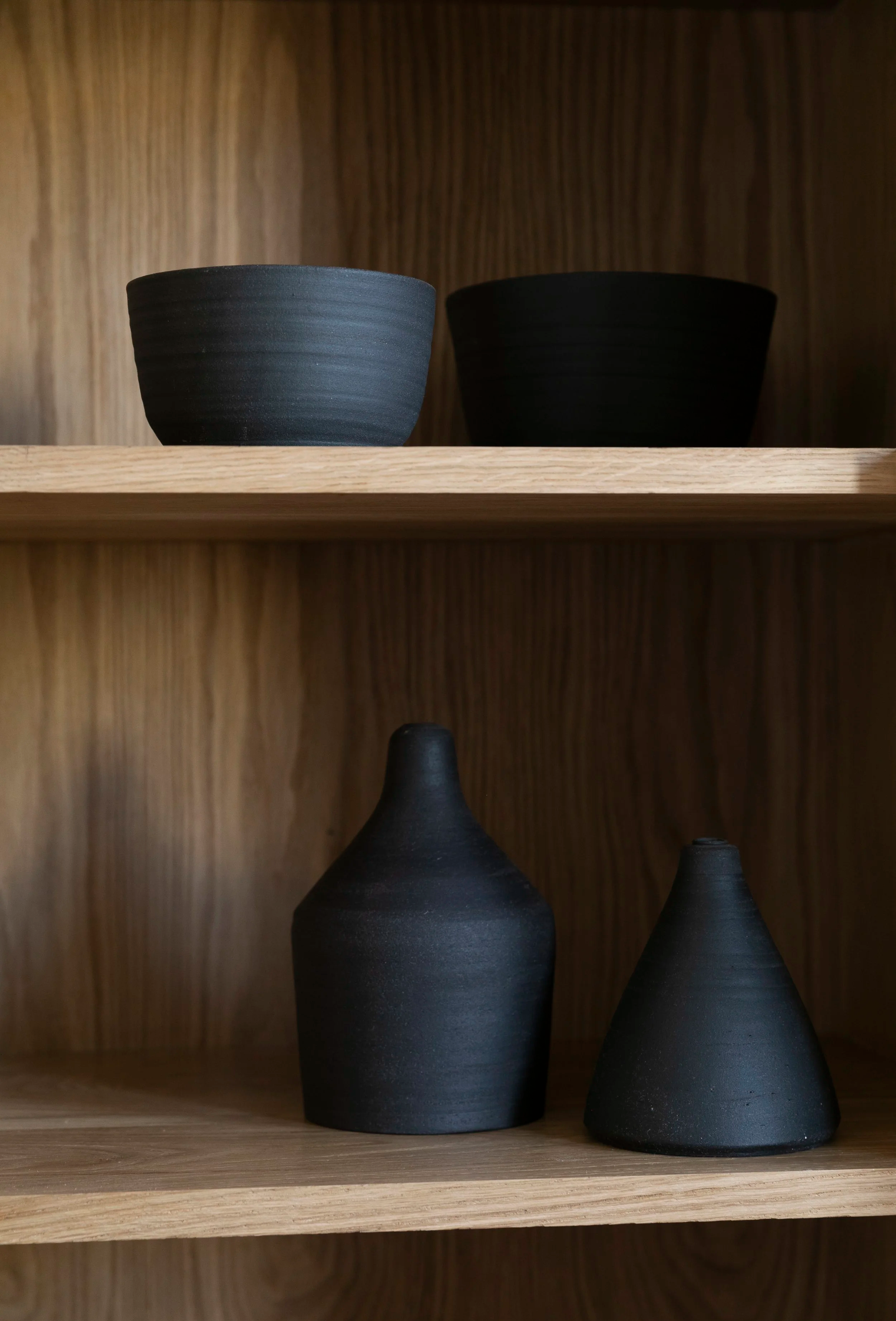 Close-up of wooden shelving holding two black ceramic vases and a black bowl.