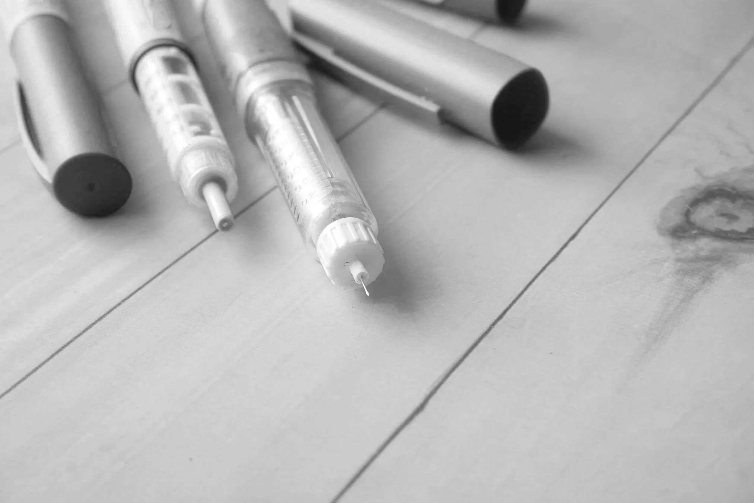 Close-up of syringes and a metal cylindrical object on a tiled floor.