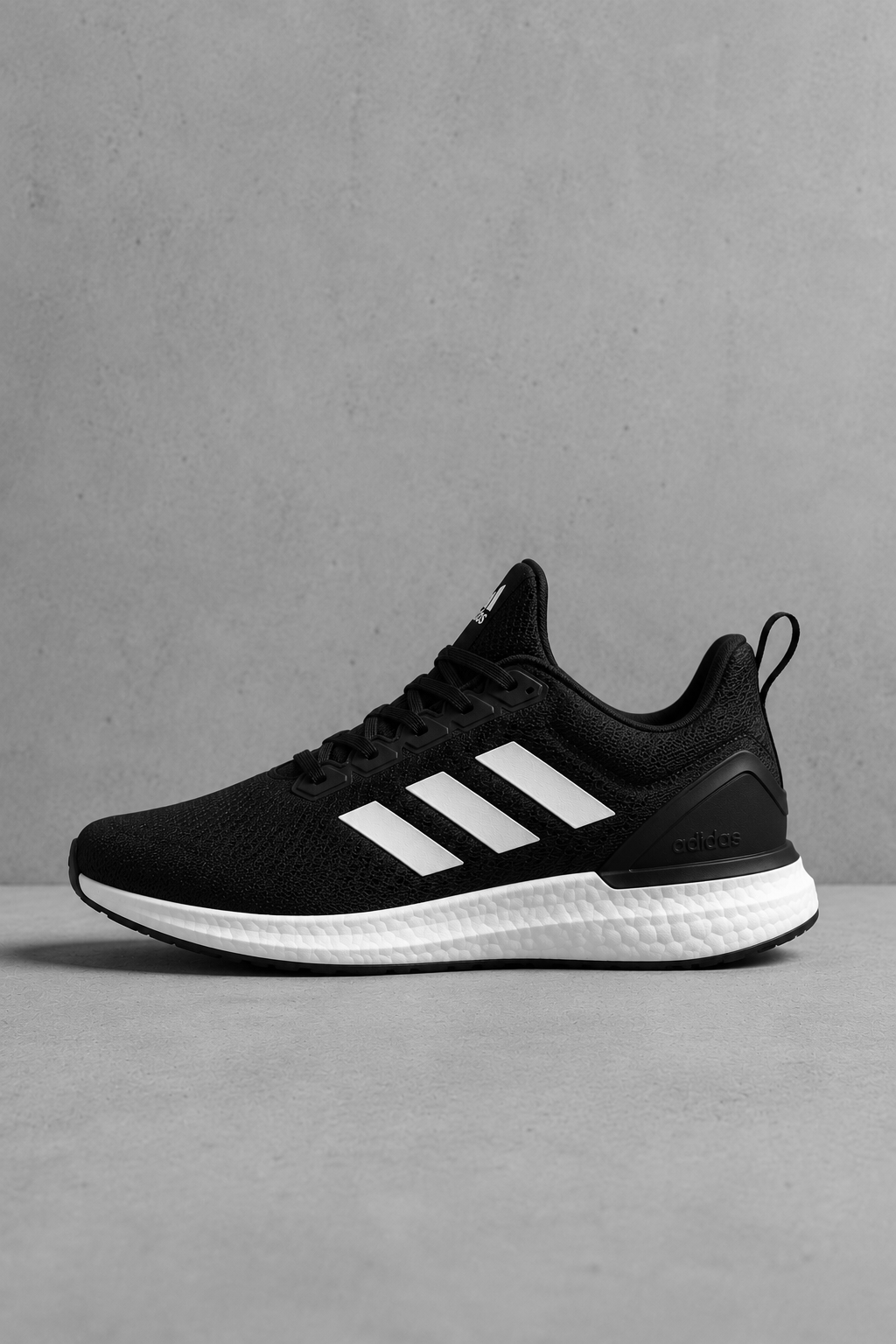 Black and white Adidas running shoe with three white stripes on the side, placed on a plain surface against a gray background.