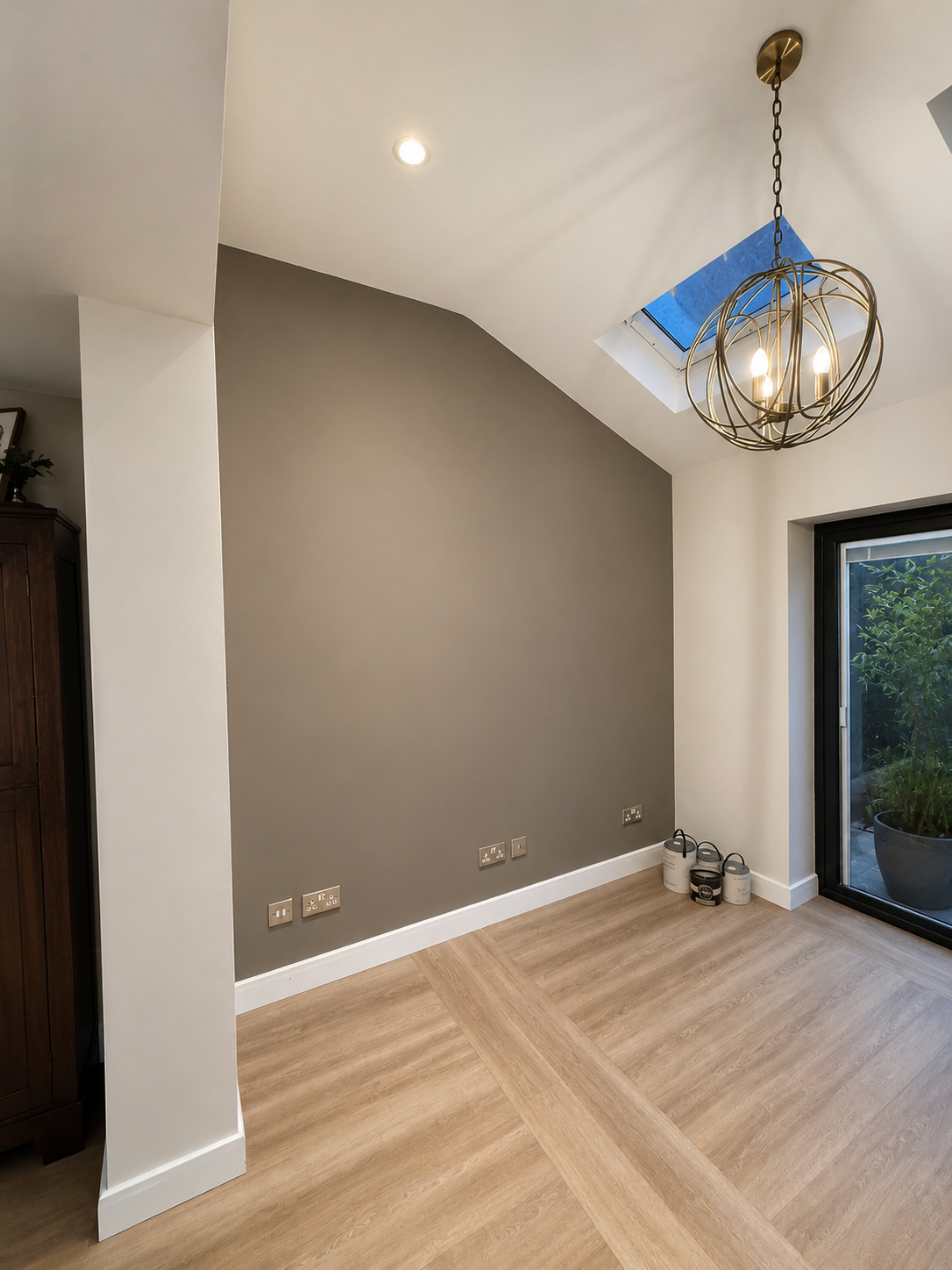Empty room with a gray accent wall, hardwood flooring, a ceiling light, a skylight, and a large sliding glass door leading to an outdoor plant.