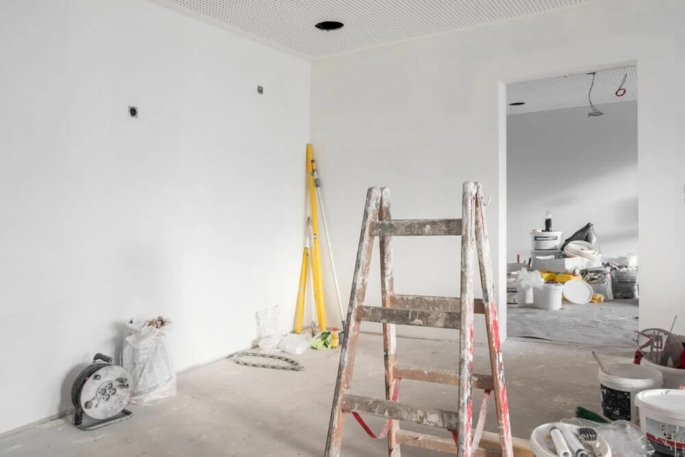 Interior room under construction with a ladder, construction materials, and tools scattered around.