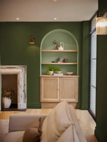 Living room with green wall, built-in shelf with decor, wooden cabinet, and beige sofa.
