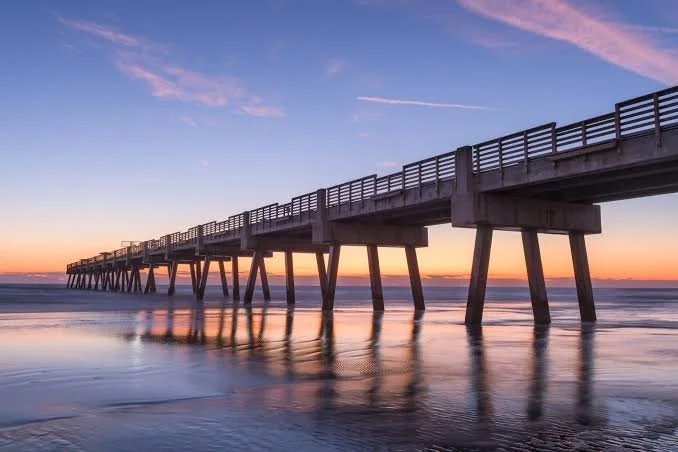 A pier extending into the ocean during sunset with a partly cloudy sky