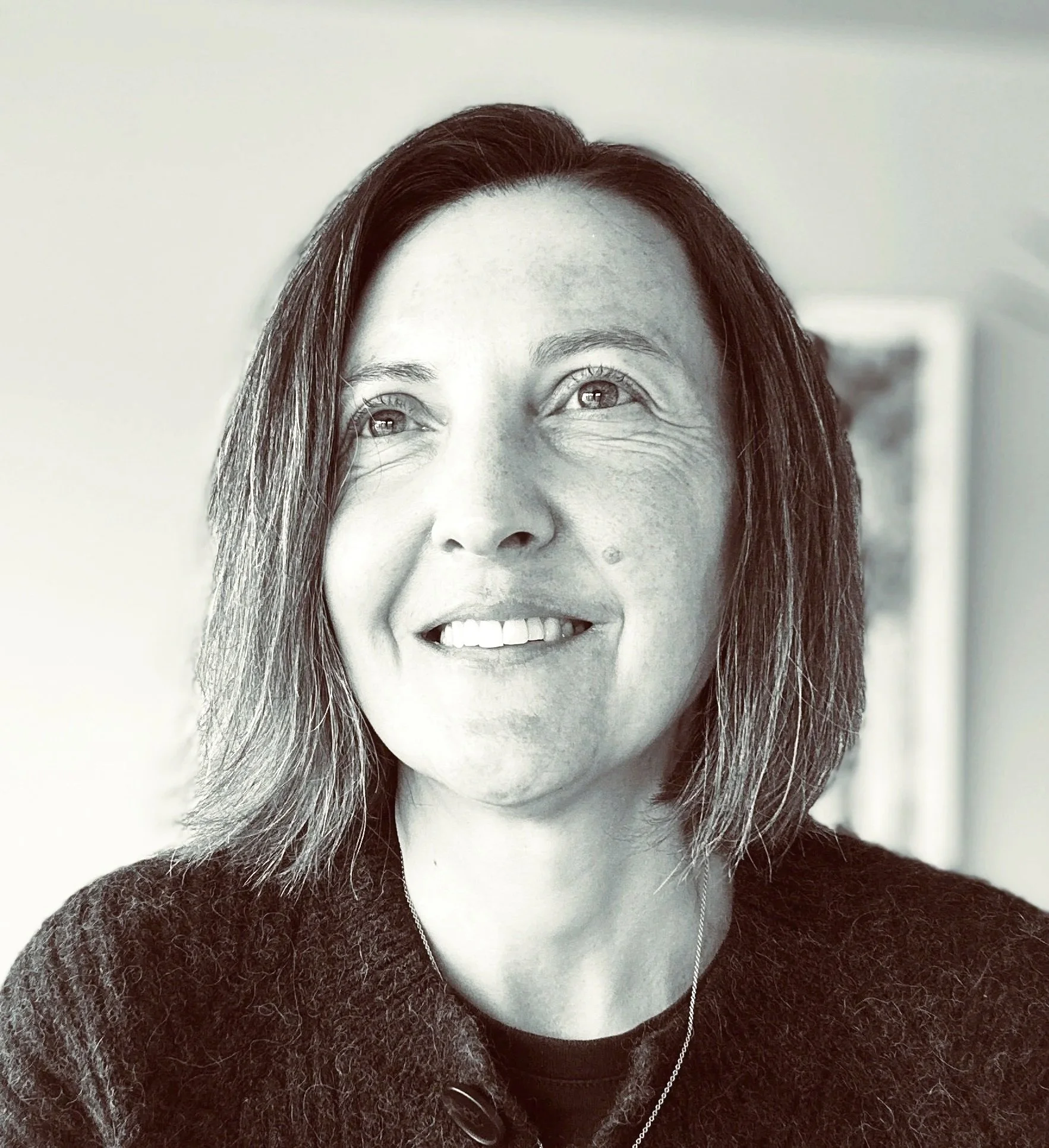 Close-up black-and-white photo of a woman with long hair, smiling and looking upwards, wearing a sweater and a necklace.
