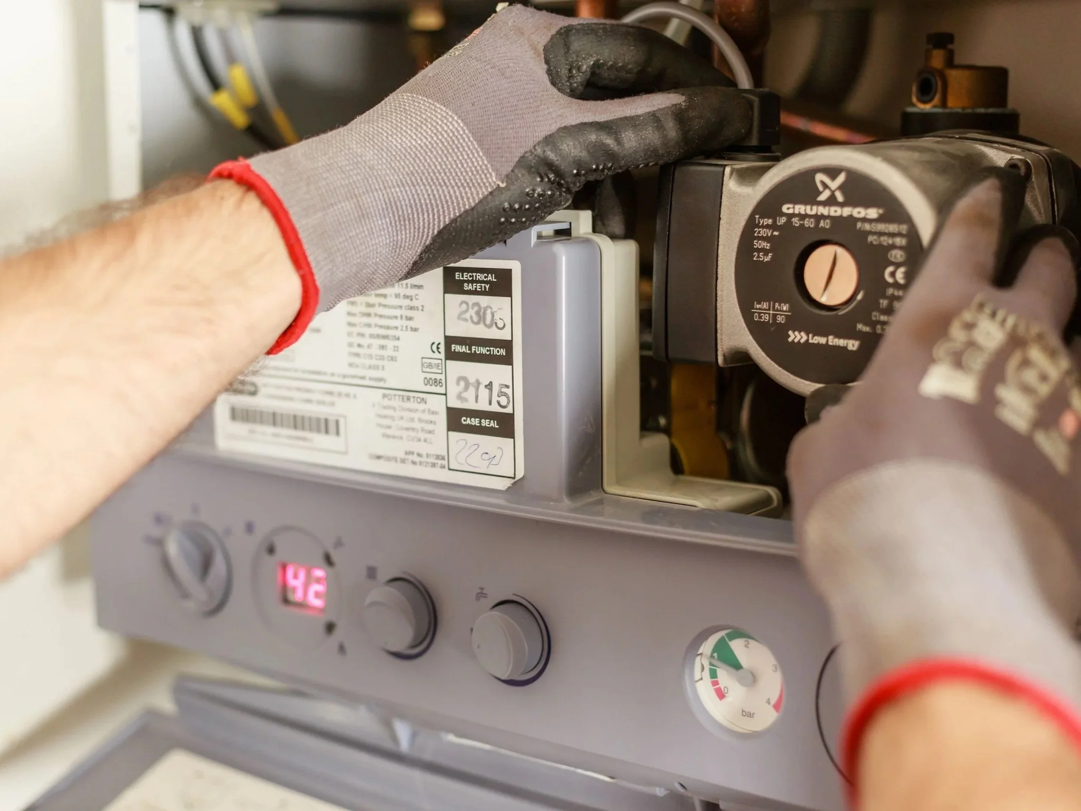 Someone wearing work gloves adjusting a Grundfos pump with a dial and electrical safety labels in an industrial or mechanical setting.