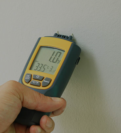 A hand holding a digital infrared thermometer pointed at a plain wall, displaying a temperature of 107.9 degrees Fahrenheit on the screen.