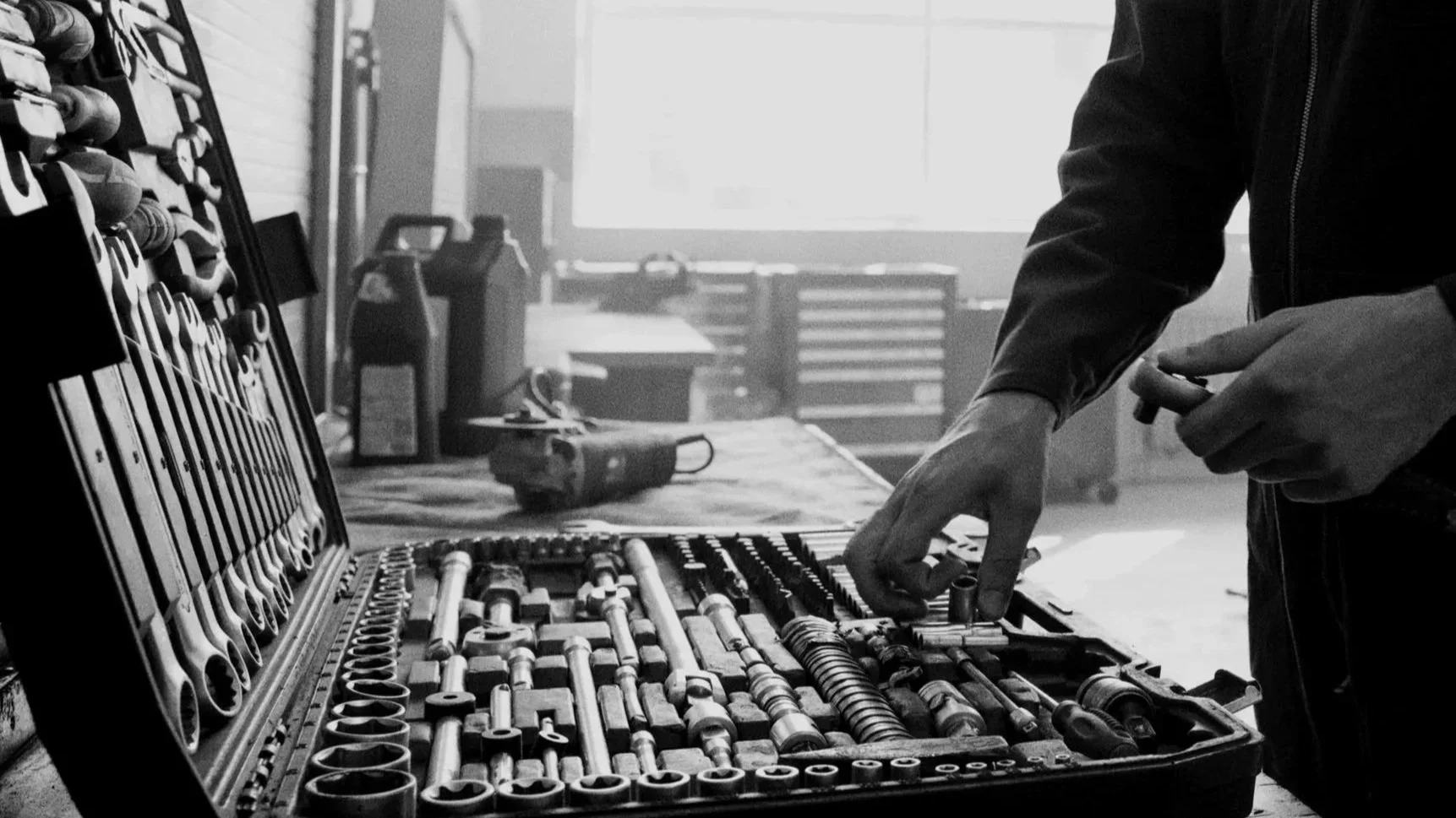 A person organizing a set of sockets and tools in a toolbox in a workshop.