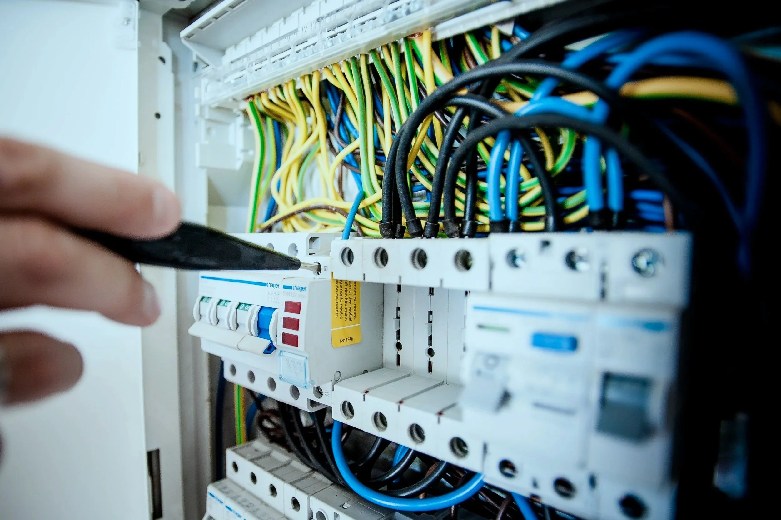 A person working inside an electrical panel with multicolored wires connected to circuit breakers.