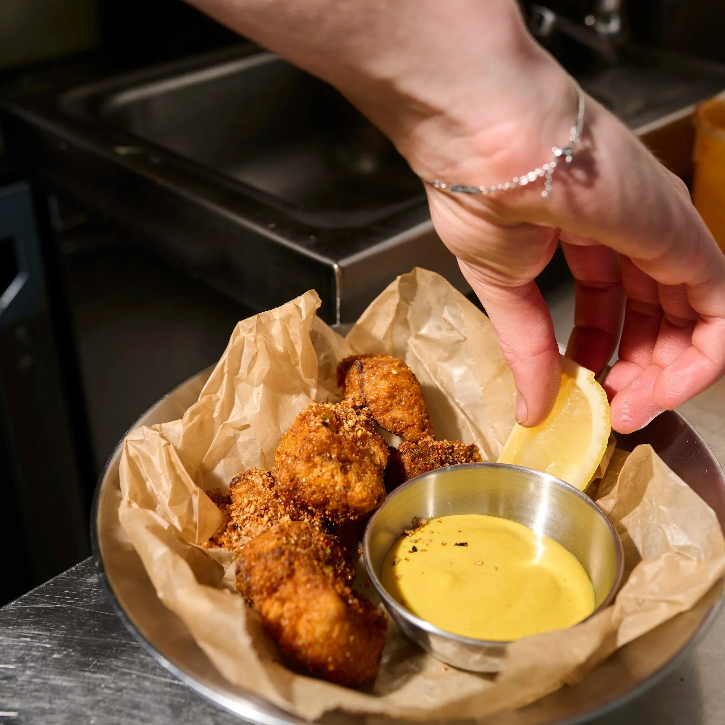 Home-made fried chicken in grease proof paper sits inside a dish with a slice of lemon and a dipping sauce