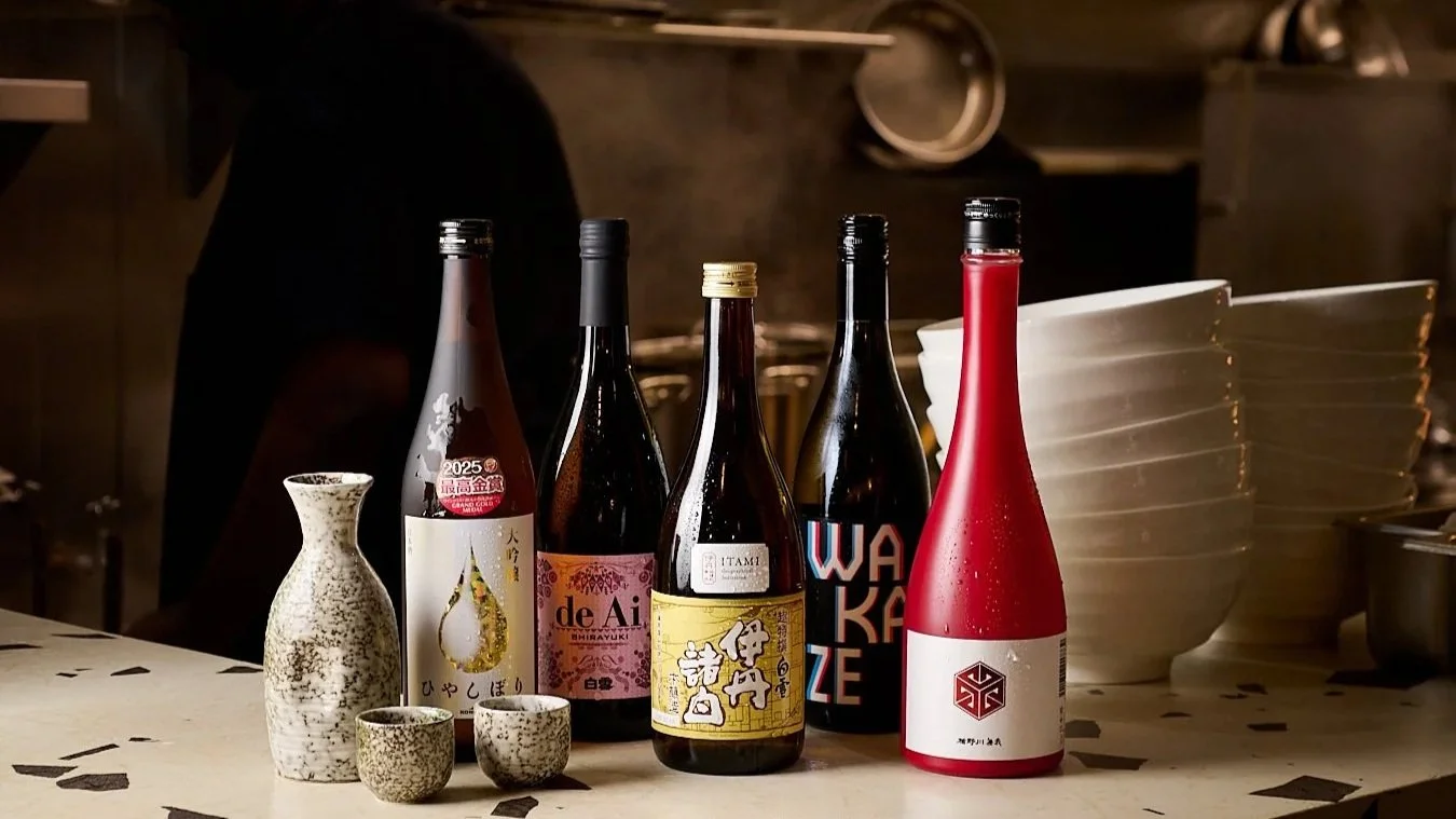 A selection of five bottles of sake and traditional sake cups on a table in a restaurant setting.