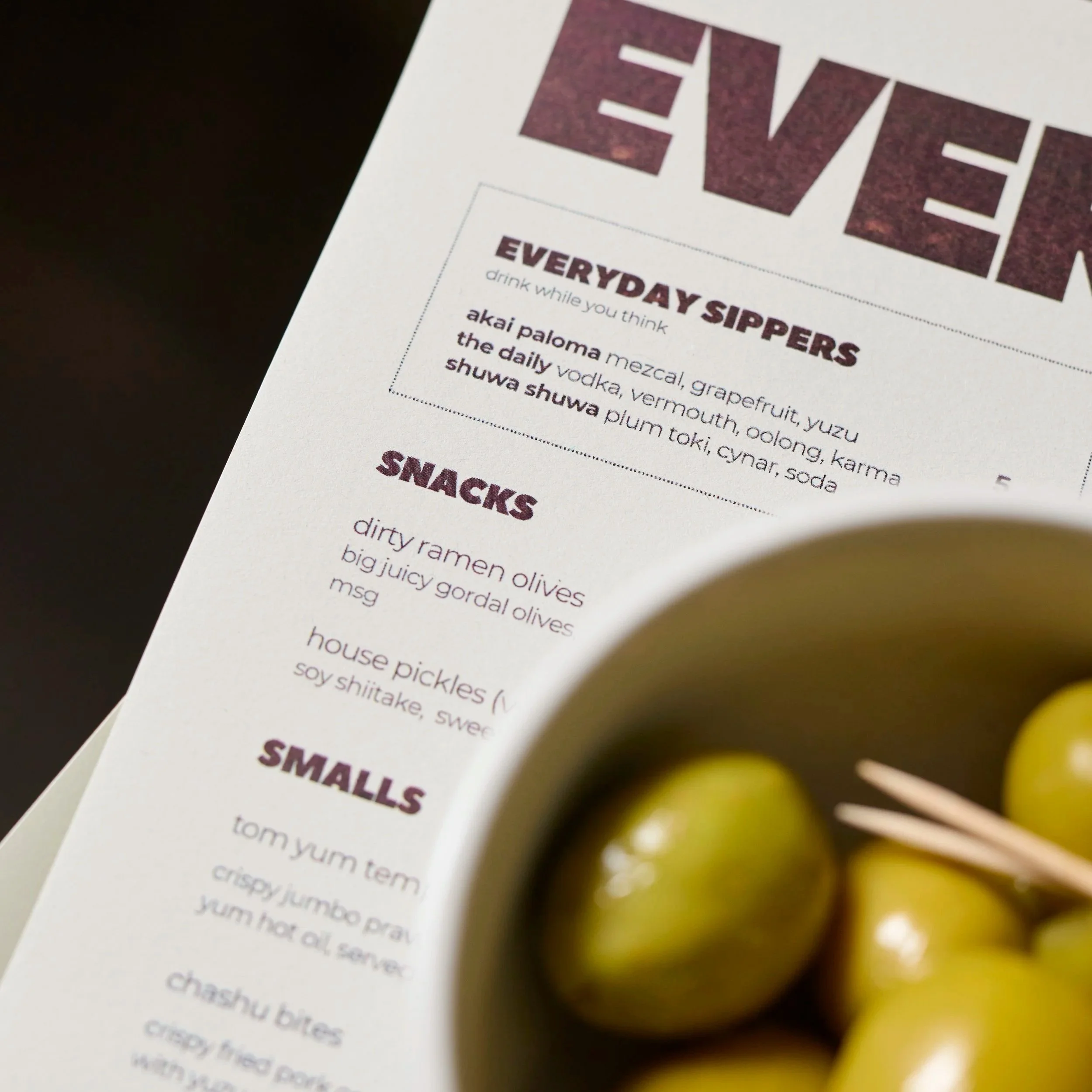 A close crop of the printed menu with an out-of-focus bowl of olives to the side.