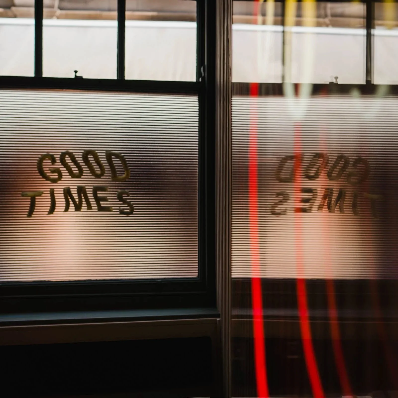 Sign writing on the window reads "Good Times" on a dark evening with a warm glow from inside behind it