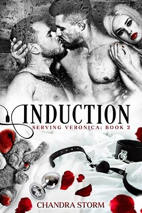 Dark romance book cover for “Induction” by Chandra Storm, featuring an intimate black-and-white scene with three figures and red rose petals scattered across silk sheets.