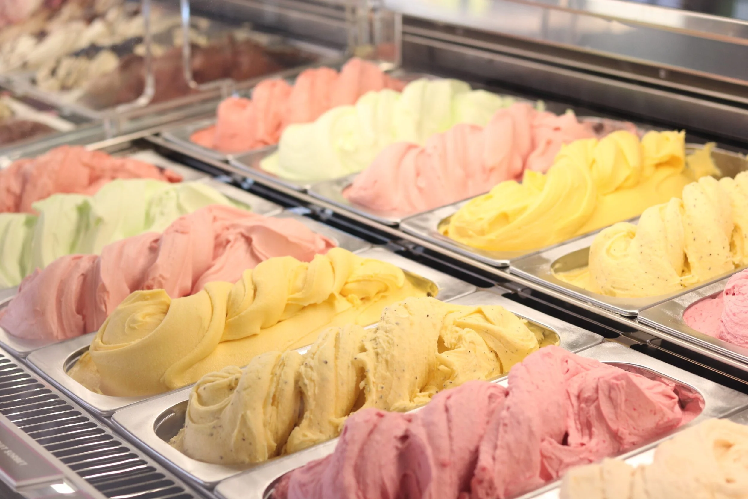 Multiple trays of colorful ice cream flavors in a display case.
