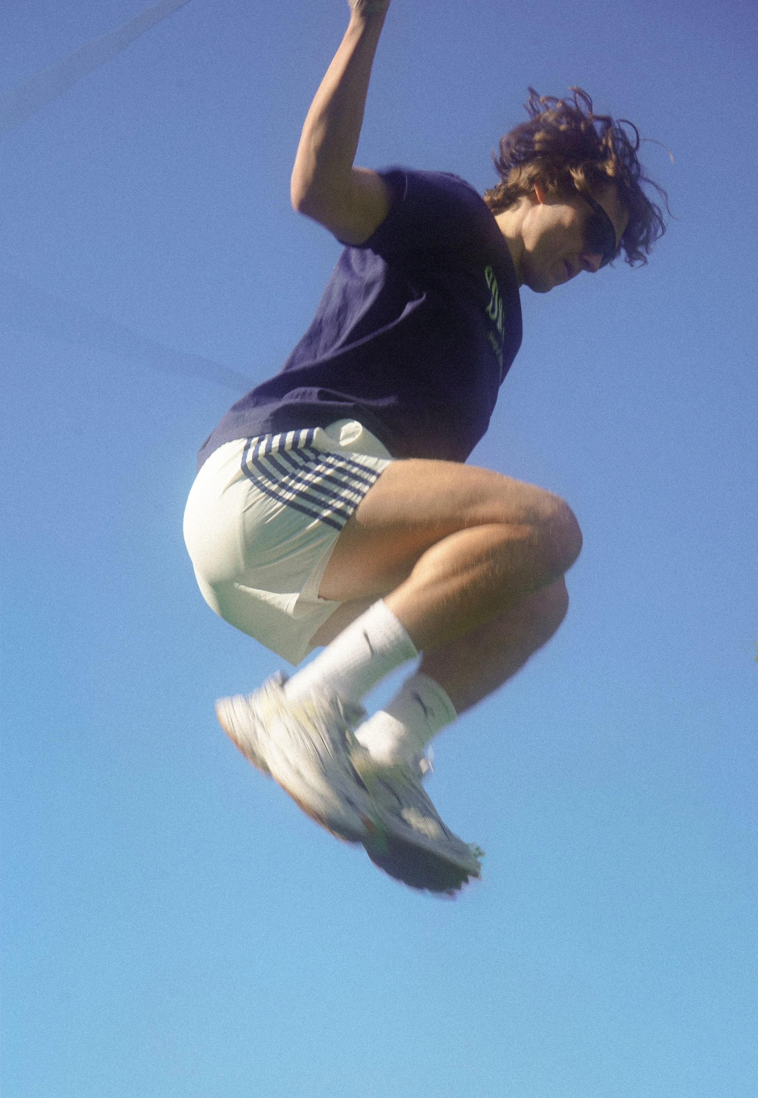 A person in athletic clothing is captured mid-air against a blue sky, possibly during a jump or athletic move.