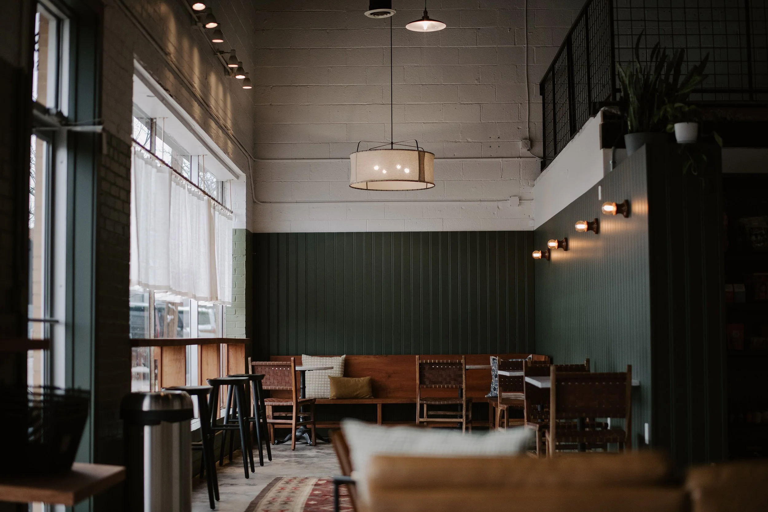 Interior of a cozy cafe with wooden furniture, pendant lighting, and large windows with natural linen curtains.