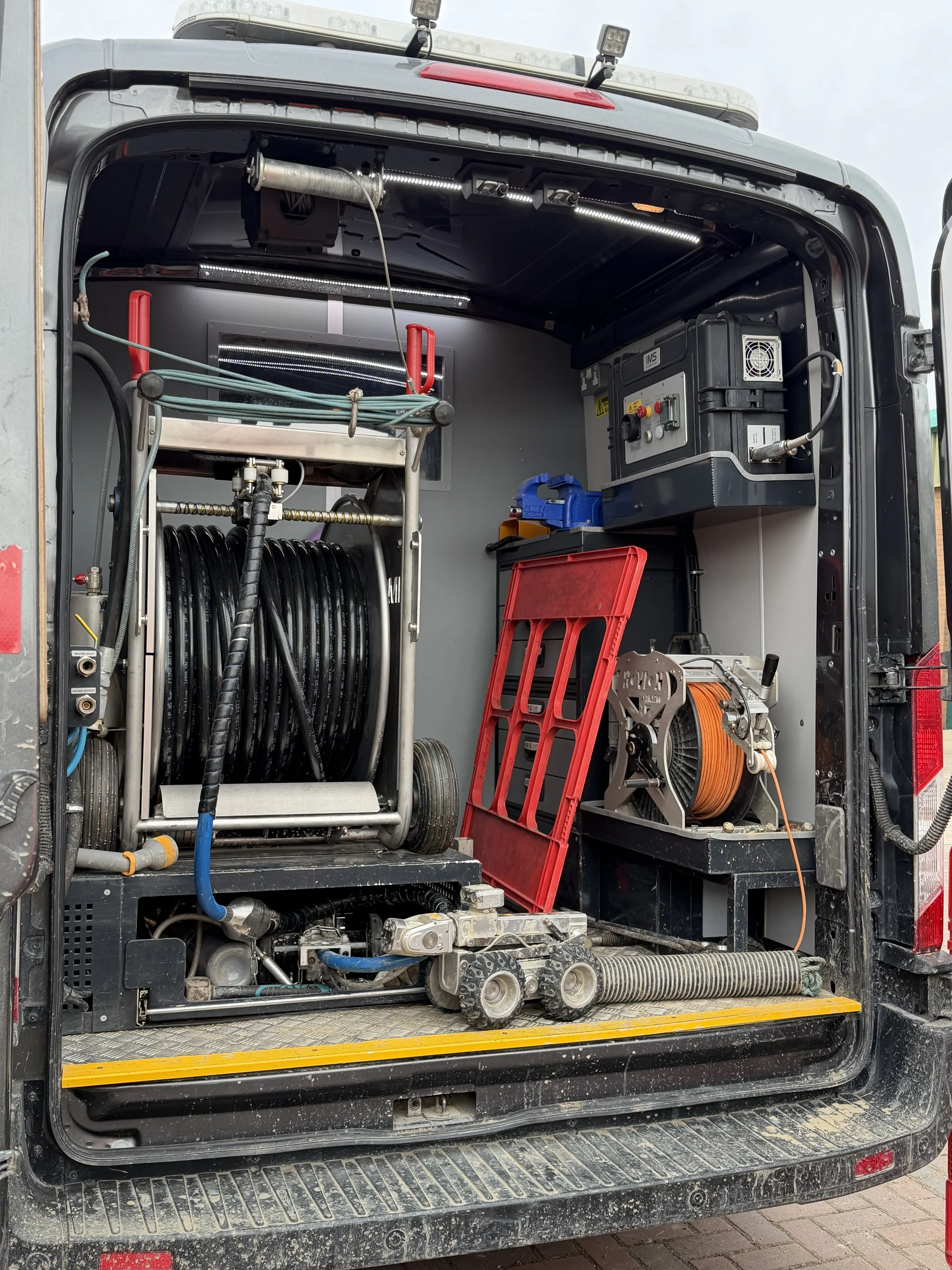 Interior of a utility truck showing equipment and tools, including hoses, cables, and a control panel.